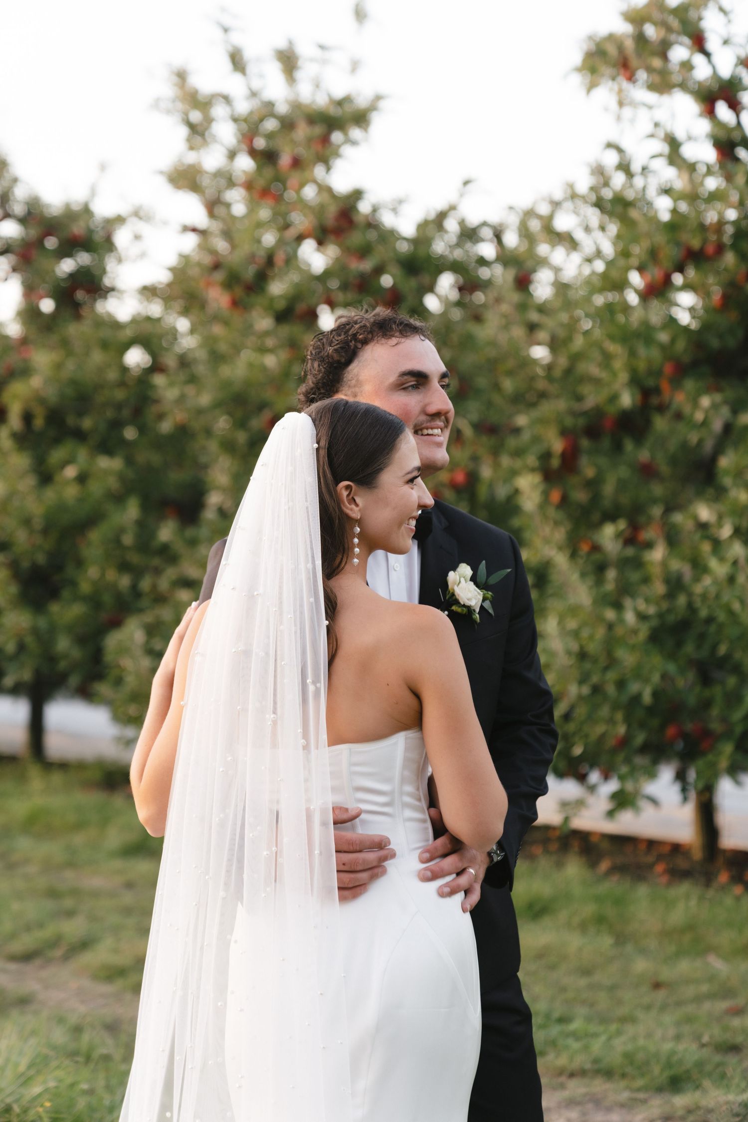 Happy couple embraces in an orchard during their wedding photoshoot.