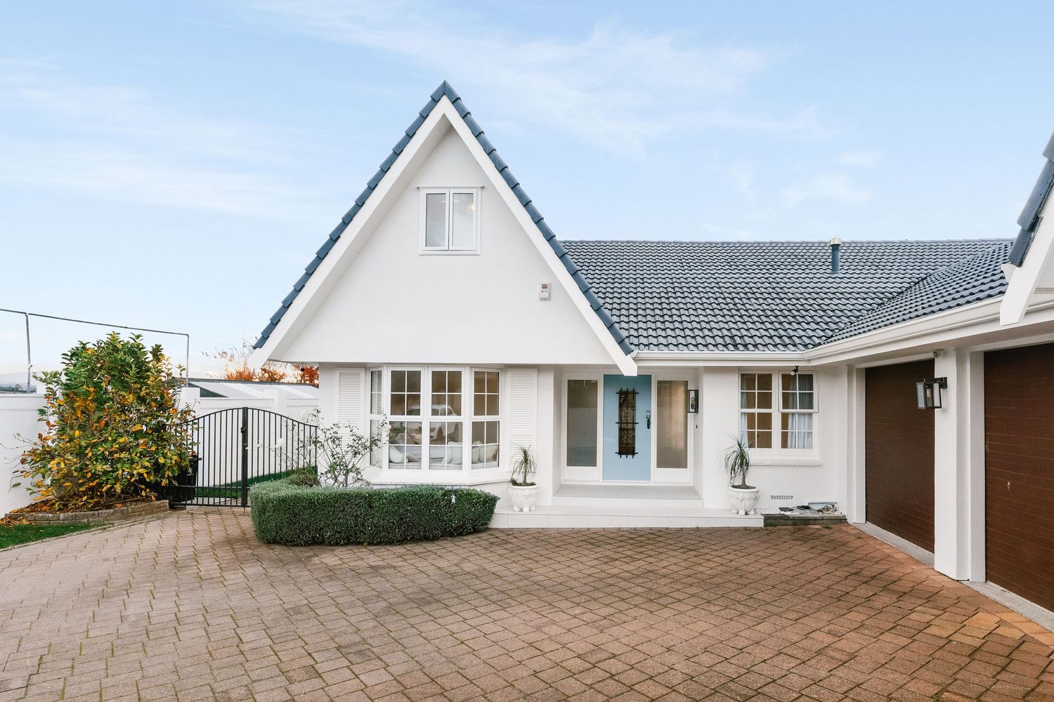 Charming A-frame house with white exterior, paved driveway and well-maintained landscaping.