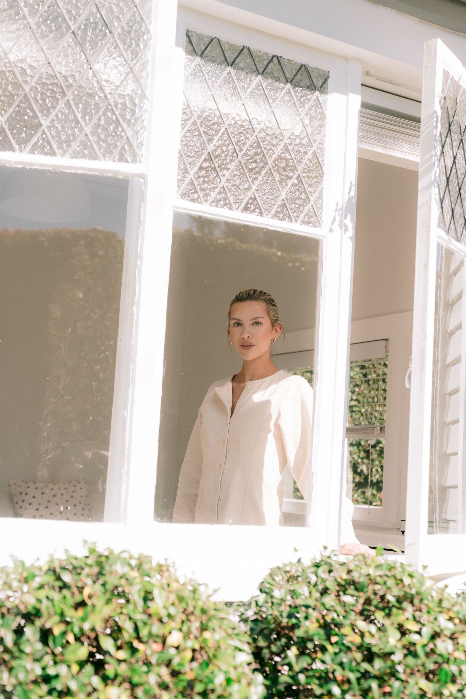 Figure in white moves gracefully along a sunlit window ledge with decorative glass panes.