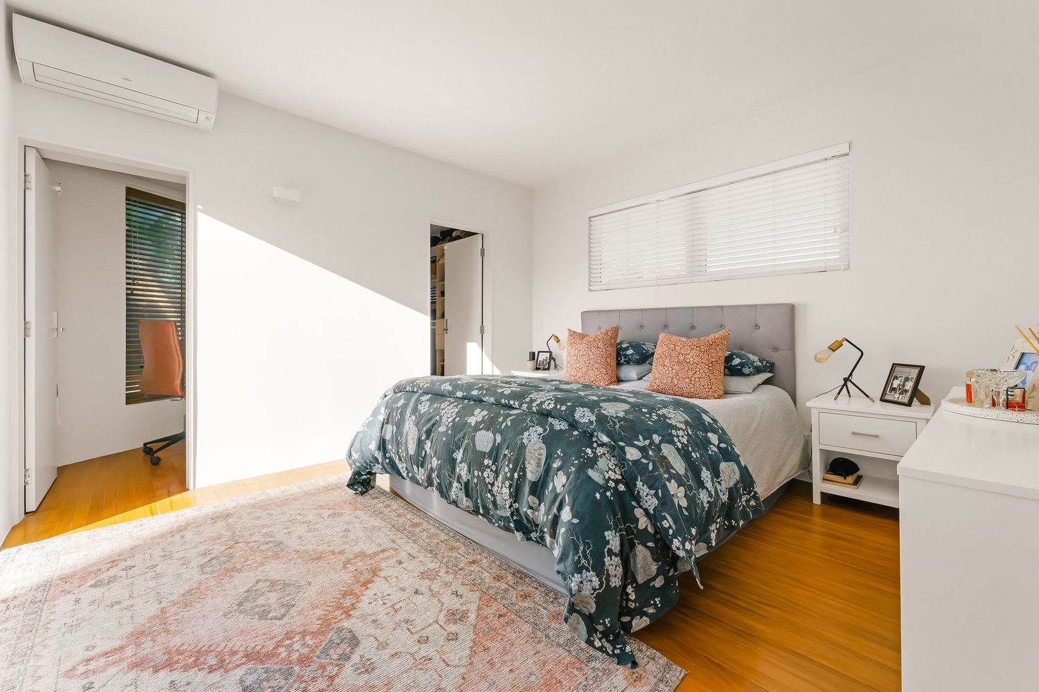Minimalist white bedroom with natural light streaming through windows and modern decor.
