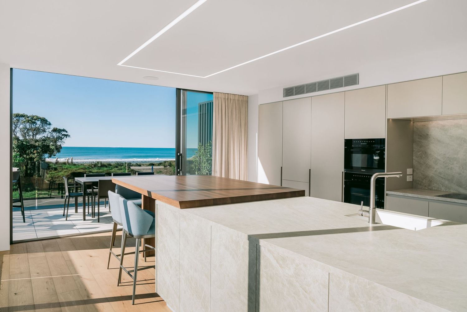 Sleek modern kitchen with white cabinetry and ocean views through large glass windows.