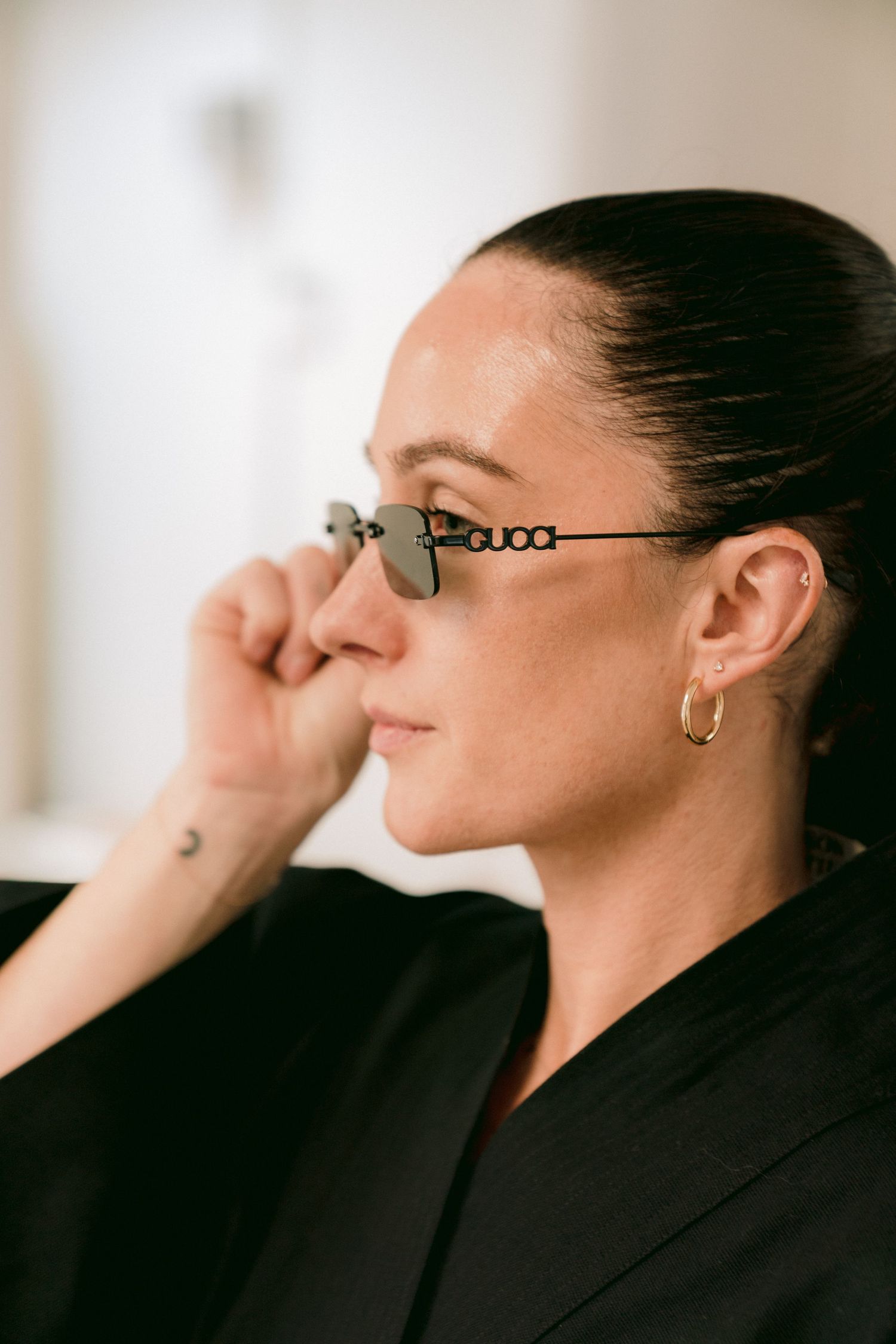 Profile view of person in black jacket and glasses touching their face against blurred background.