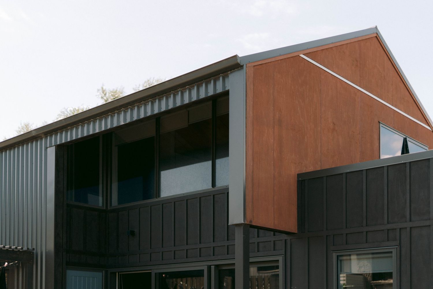 Modern industrial building complex with angular brown metal panels and dark gray accents against clear sky.
