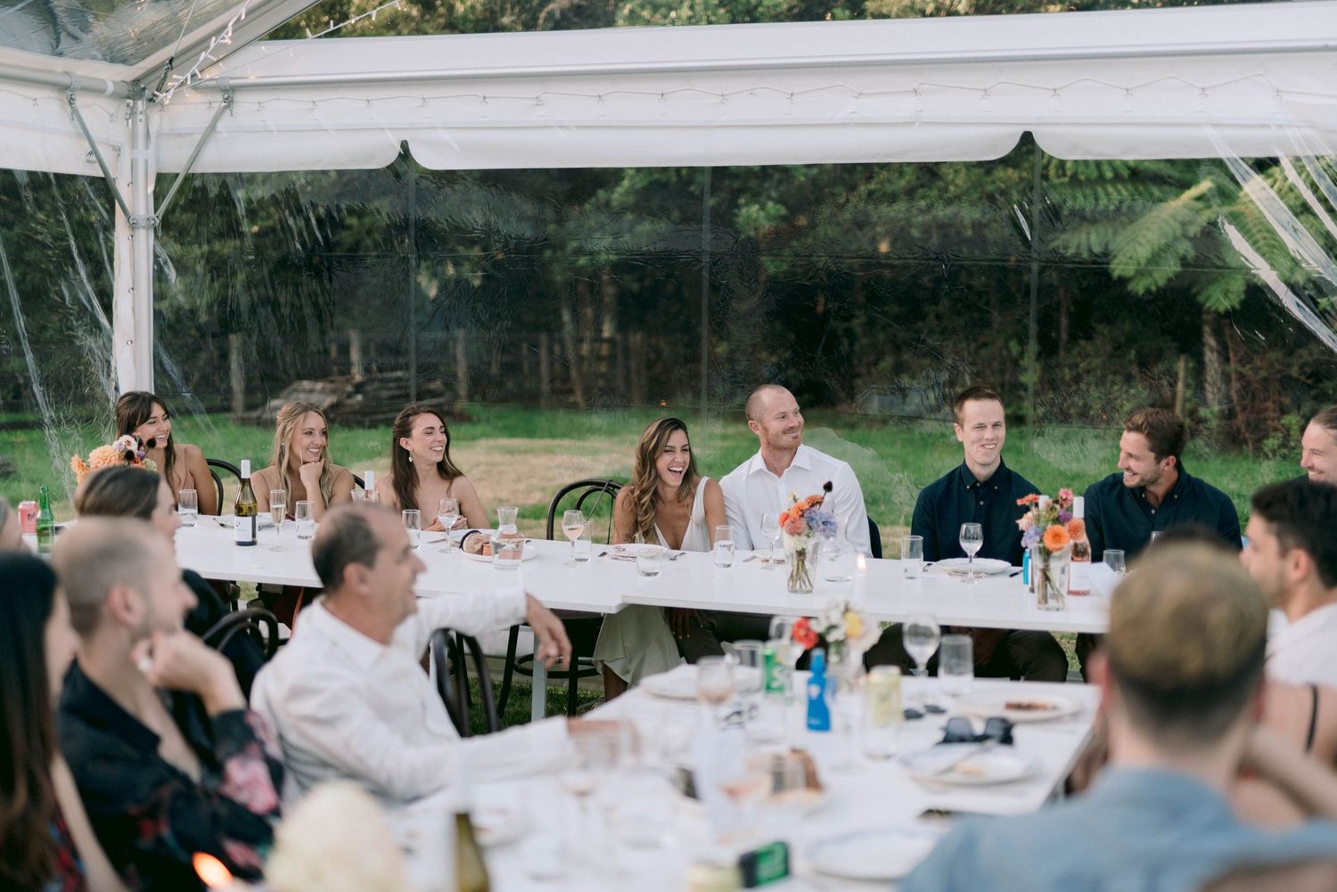 Wedding guests gathered under a white tent for an outdoor reception dinner.