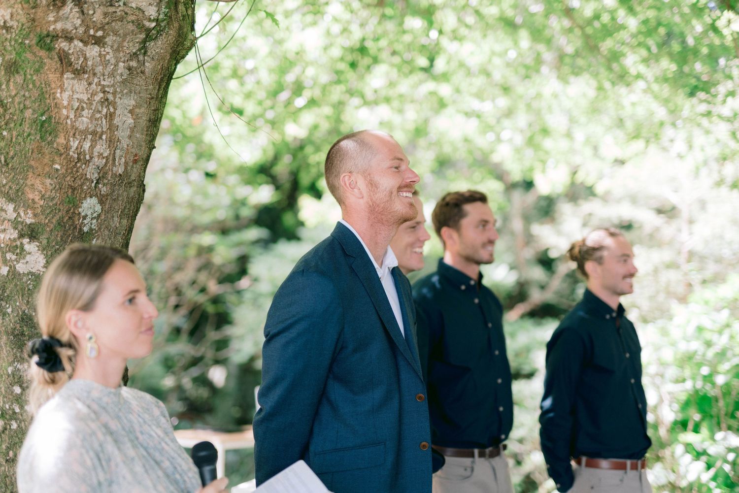 A group stands outdoors beneath a large tree during a ceremony.