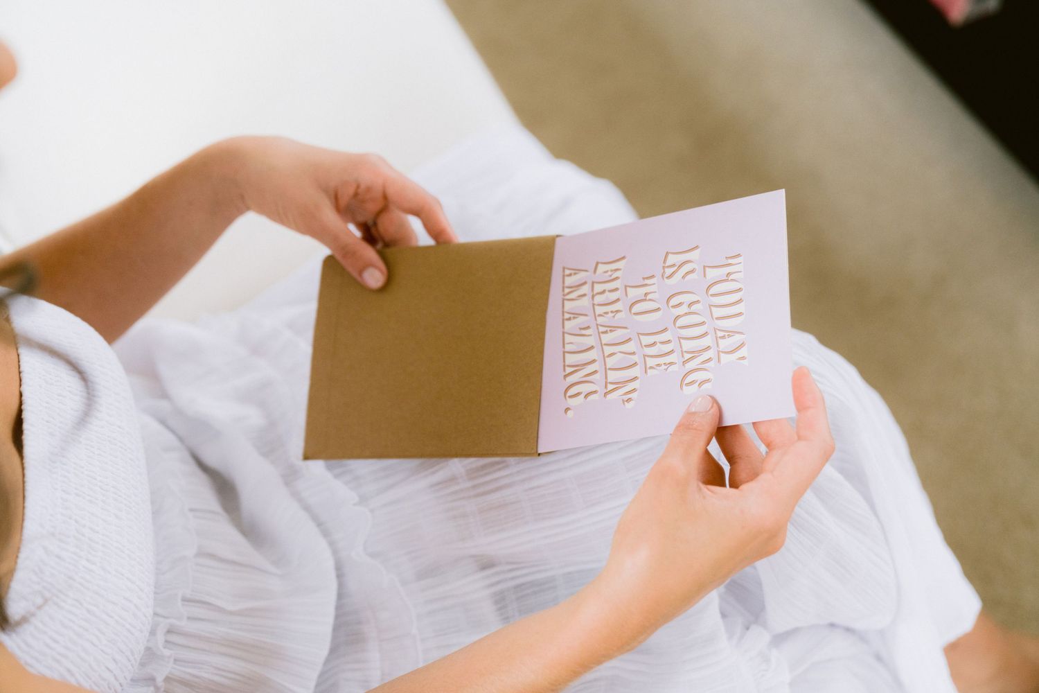 Hands holding a brown and white card with repeating text pattern against a light fabric background.