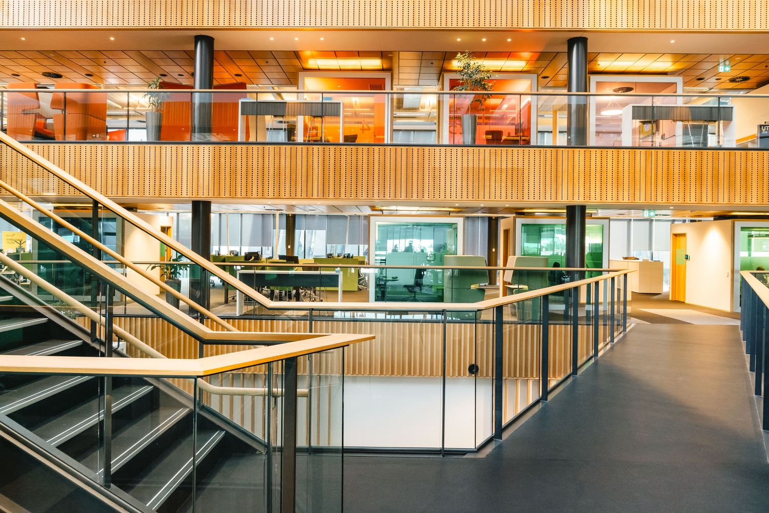 Modern office interior with wood accents features glass railings, metal staircases and open layout design.