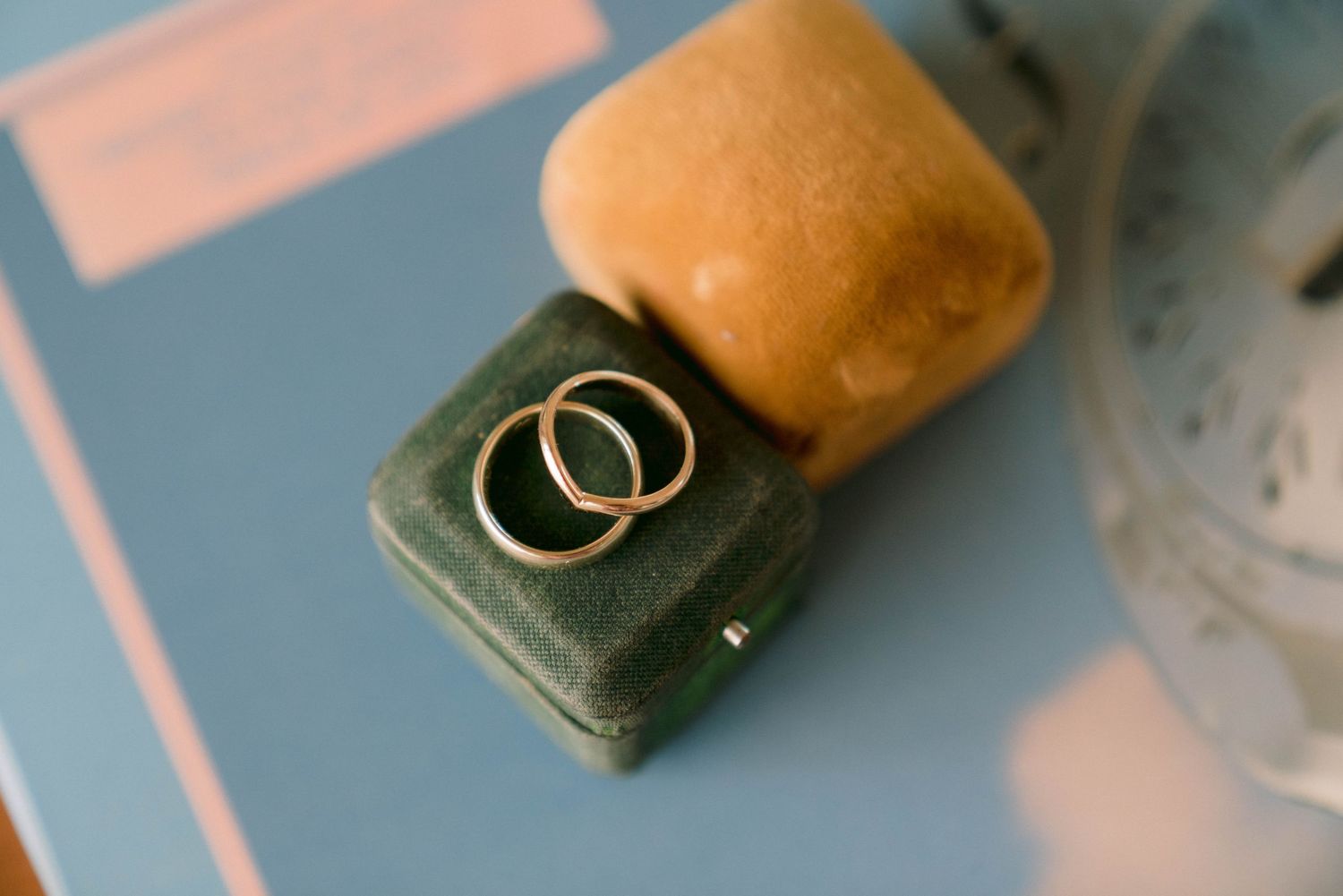 Two wedding rings displayed on velvet ring boxes against a blue surface.