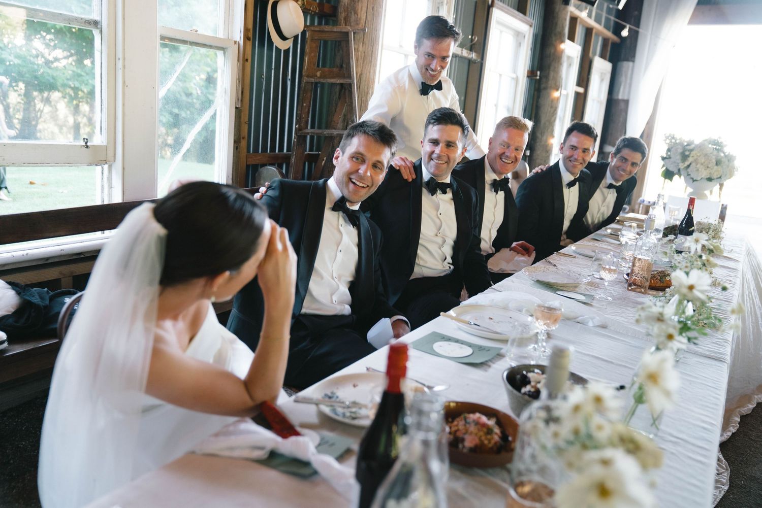 Bride and groomsmen sharing a candid moment while sitting at an elegantly set wedding reception table.