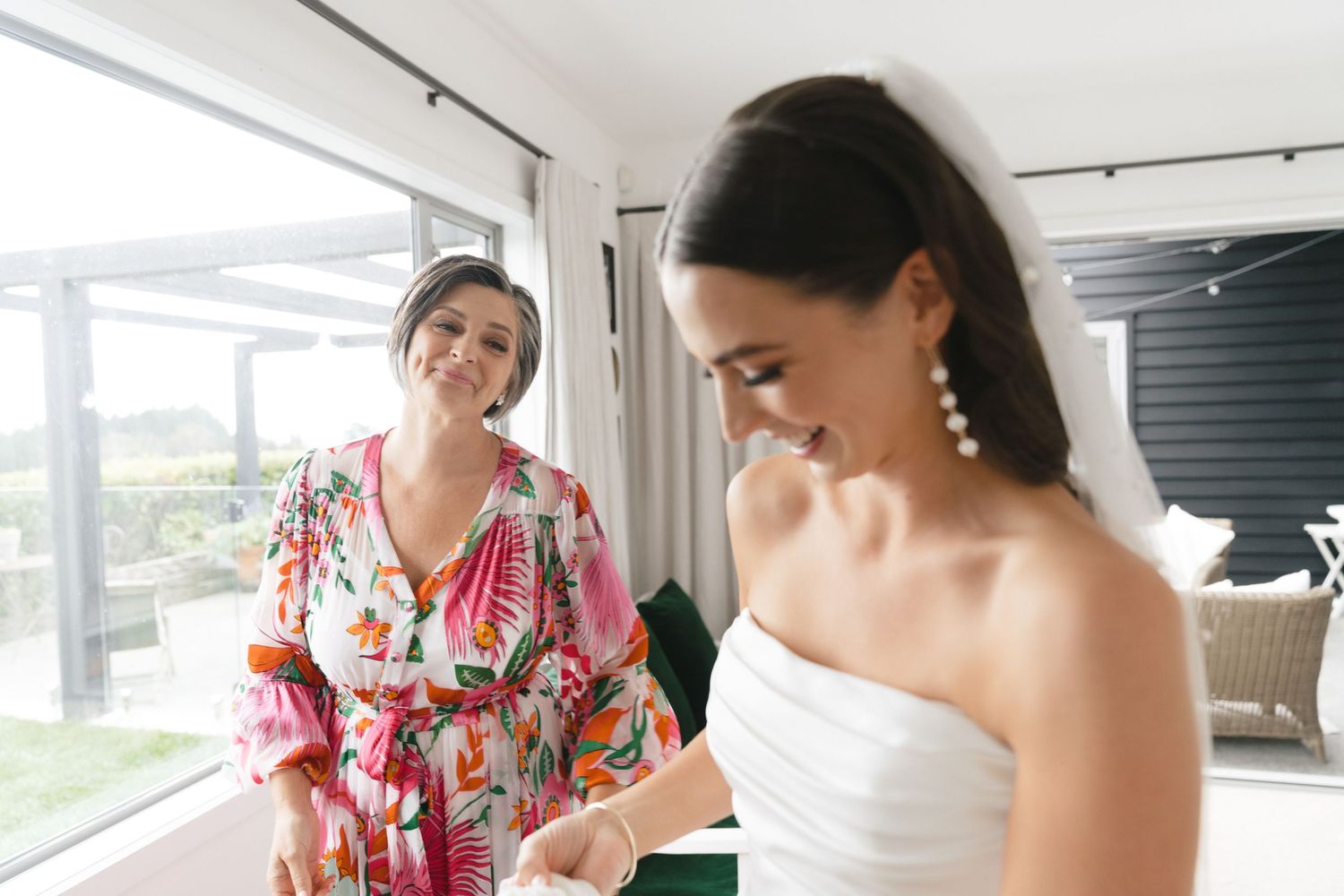 Inside a bright room, two people share a joyful moment while getting ready, one wearing a colorful floral robe.