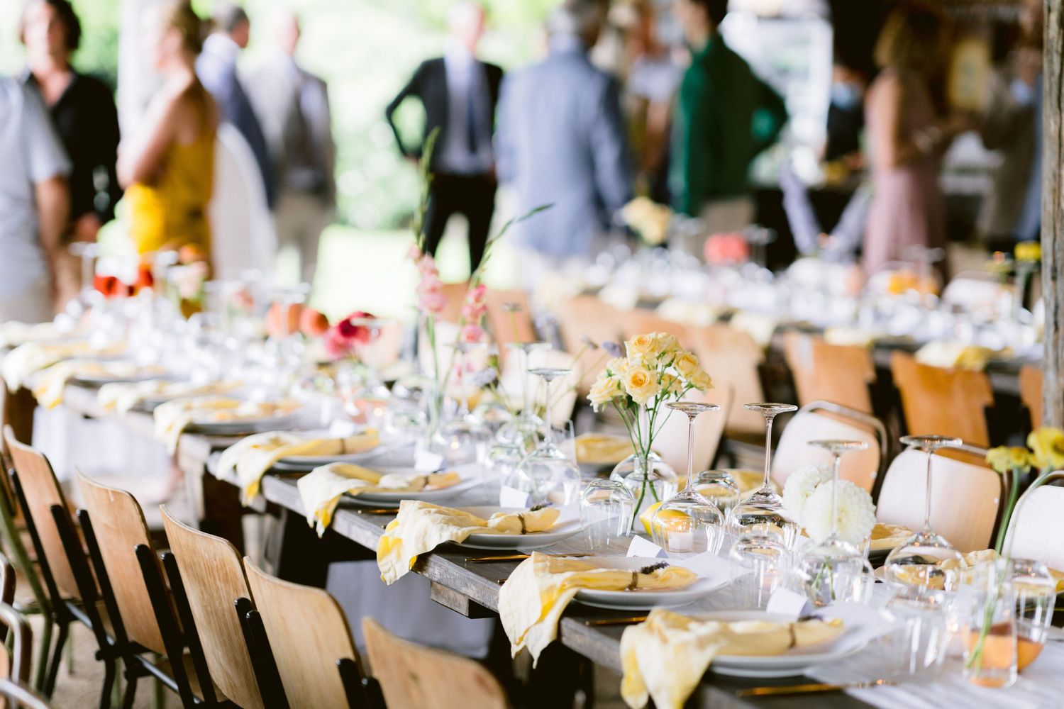 Elegant outdoor wedding reception table setup with glassware, flowers and rustic wooden chairs.