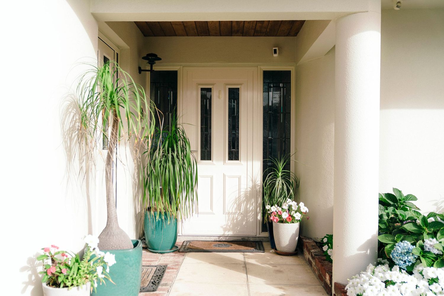 A welcoming front porch entrance with potted plants and a white door surrounded by windows.