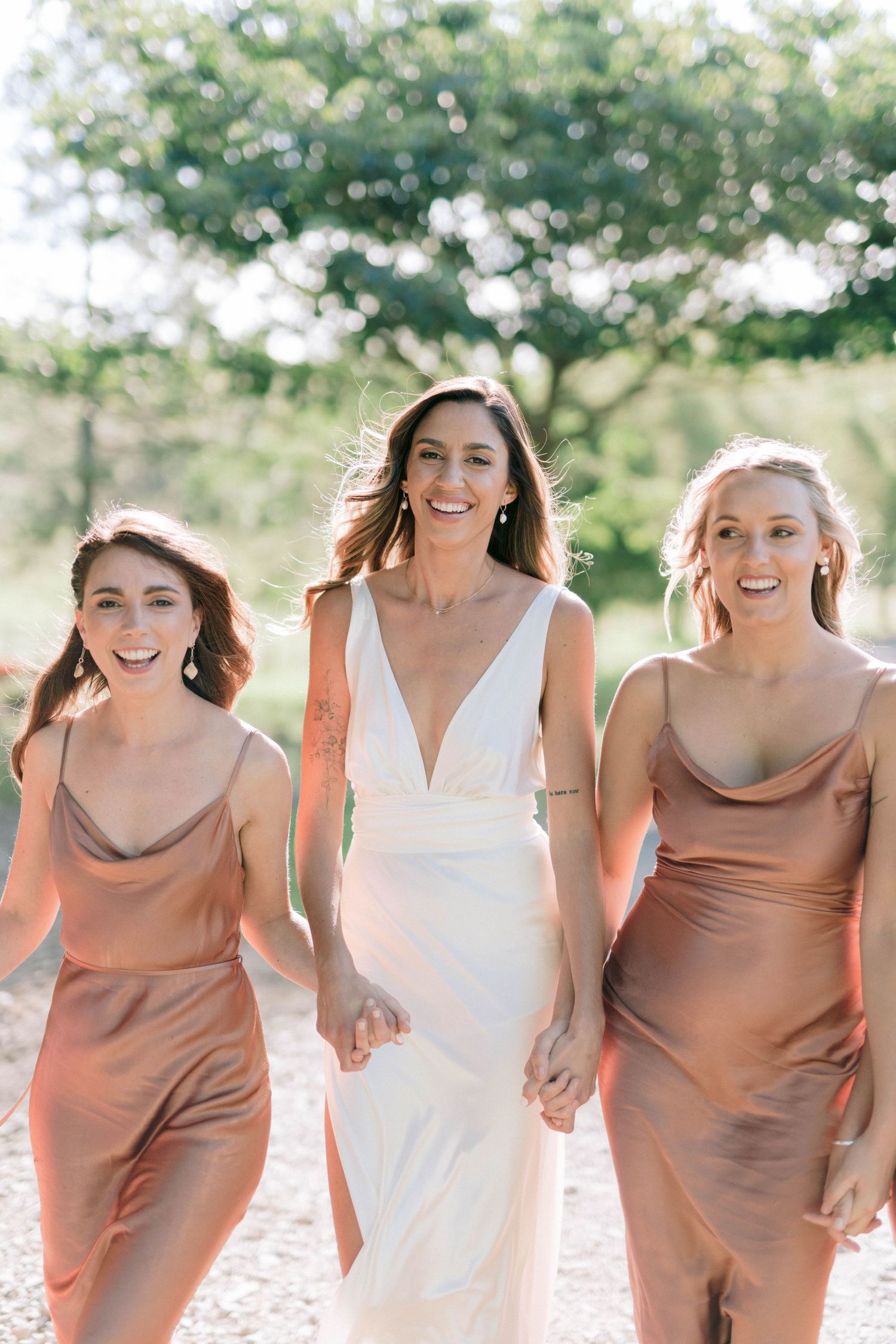 Bridesmaids in blush dresses walking together outdoors during wedding photos.