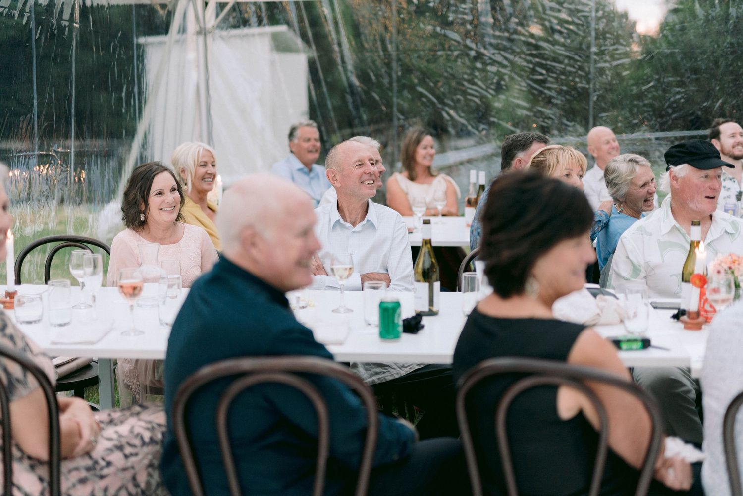 Wedding reception guests seated at long tables under string lights outdoors.