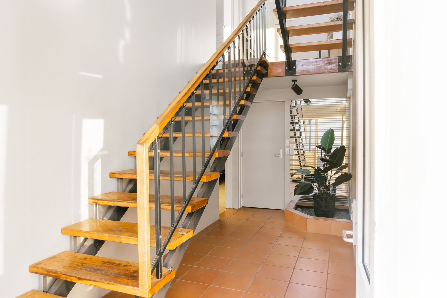 Floating wooden staircase with metal railings and terracotta floor tiles in a white hallway.