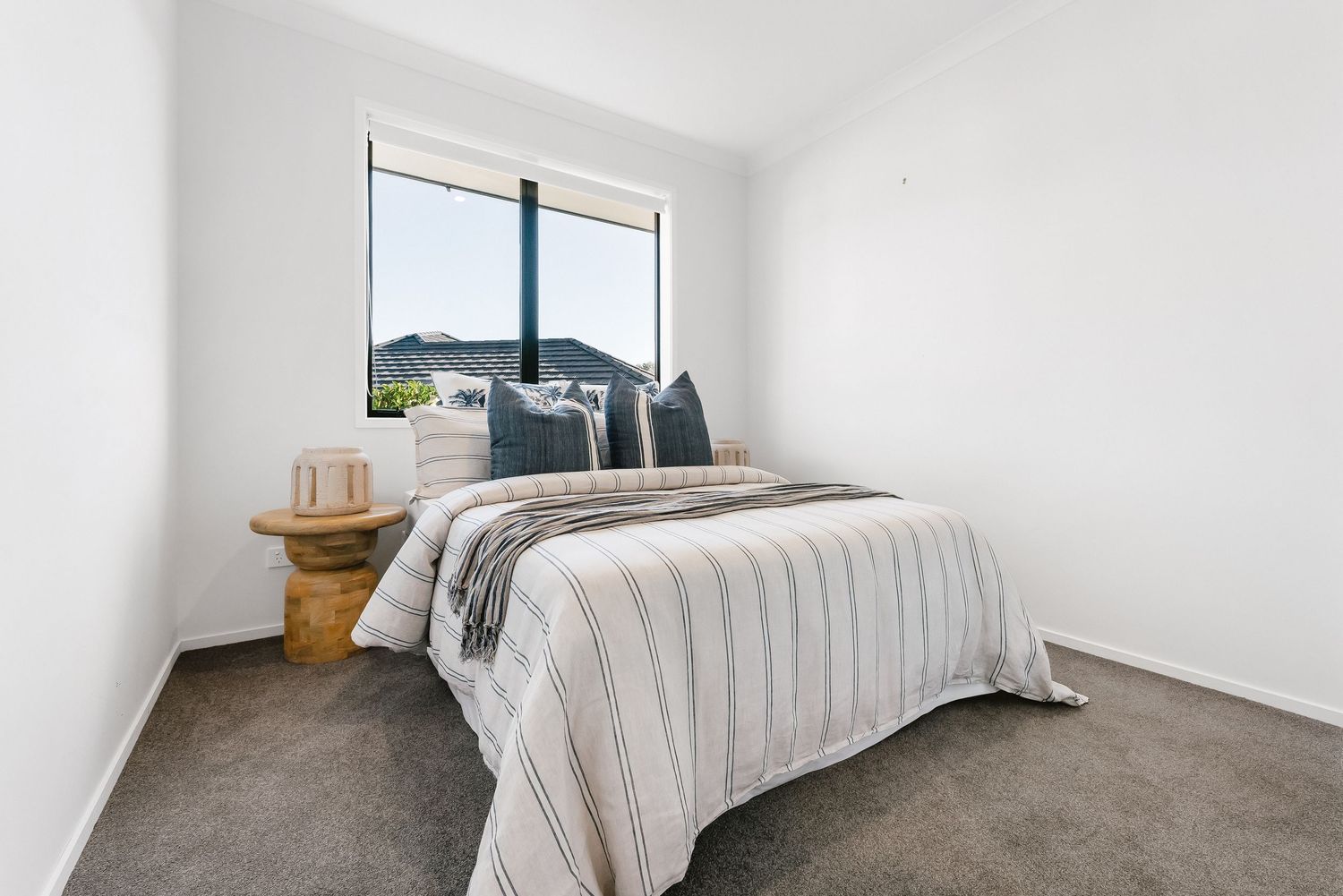 Modern bedroom interior with white walls, plush grey bedding, and a window offering mountain views.