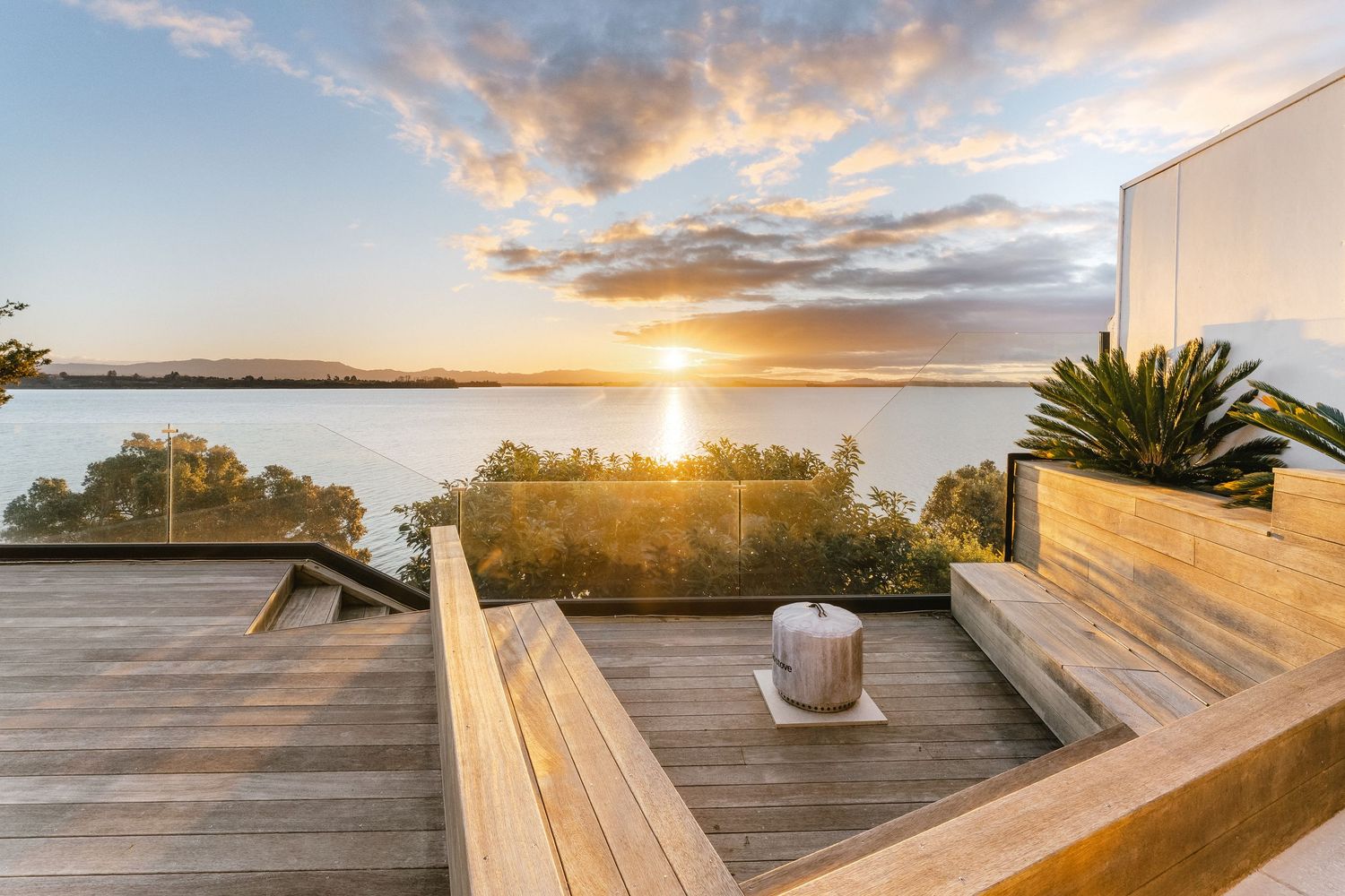 Wooden deck terrace with built-in seating overlooking water view during golden sunset.