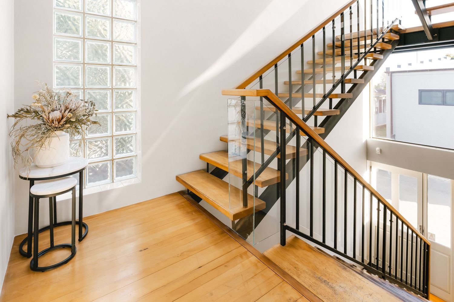 Modern wooden staircase with black metal railings and glass panels in a bright interior space.