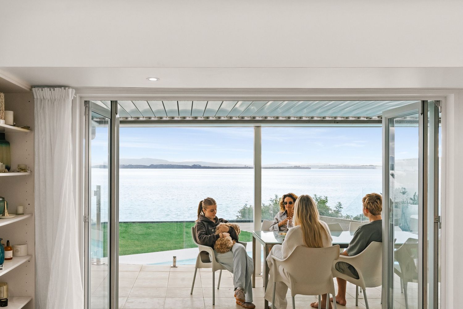 Waterfront dining area with large windows overlooking the ocean and comfortable seating for a group.