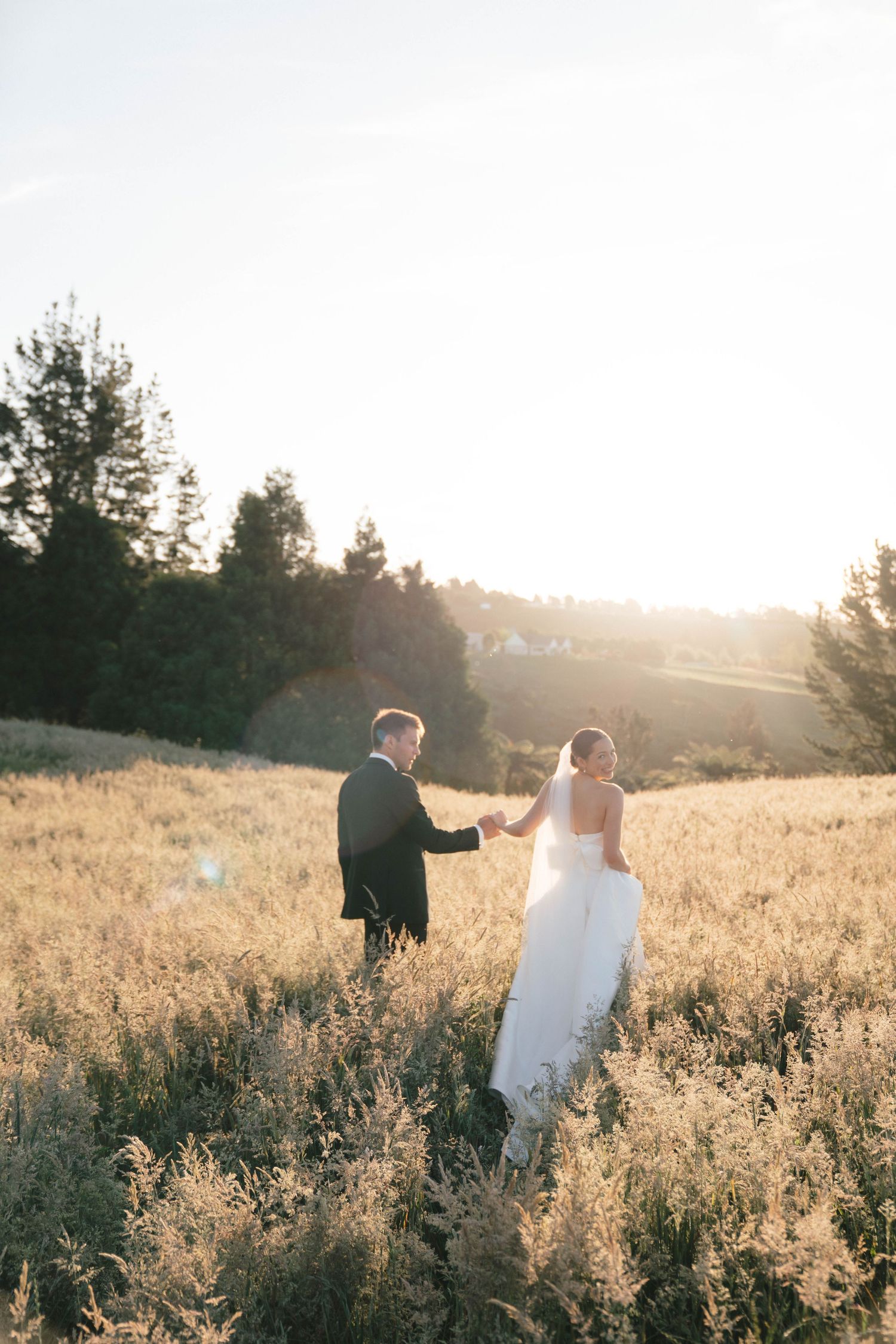 Newlyweds walking through a golden field at sunset during their outdoor wedding photoshoot.