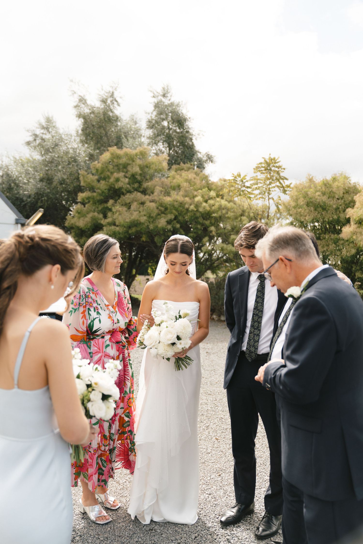 Wedding party gathered outdoors with bride holding white bouquet.