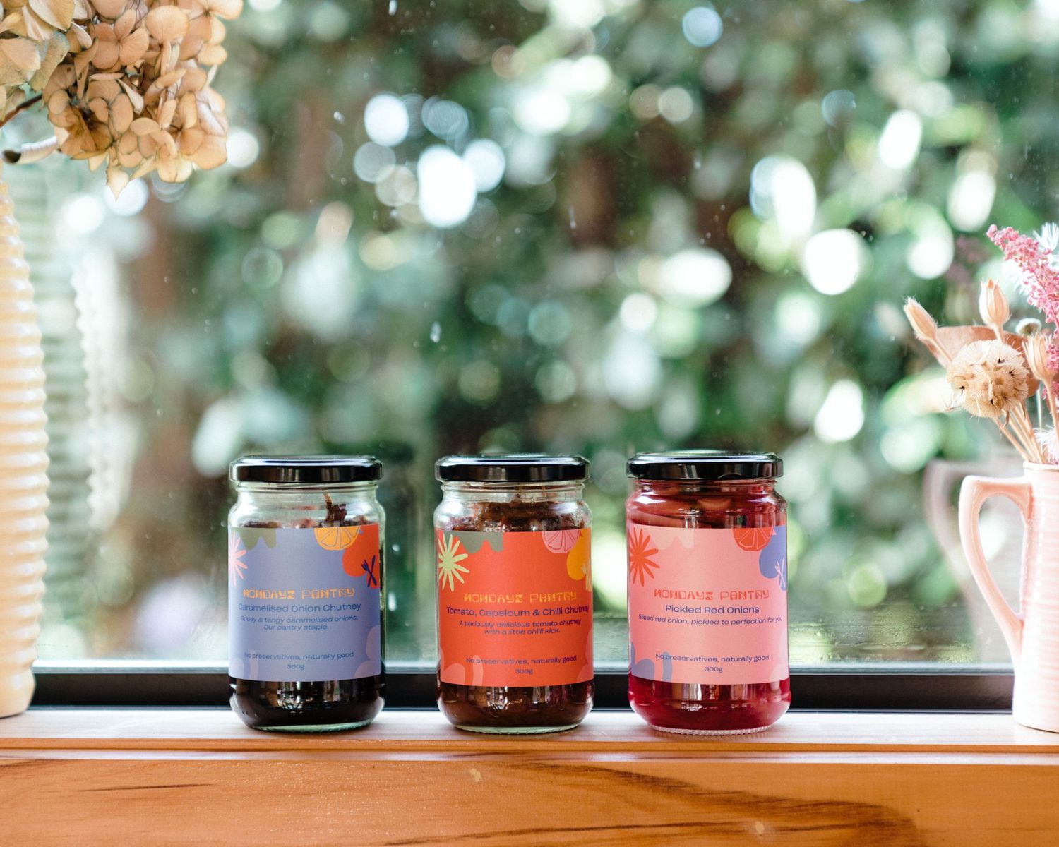Colorful glass jars with lids arranged in a row on a window sill with natural light and bokeh background.