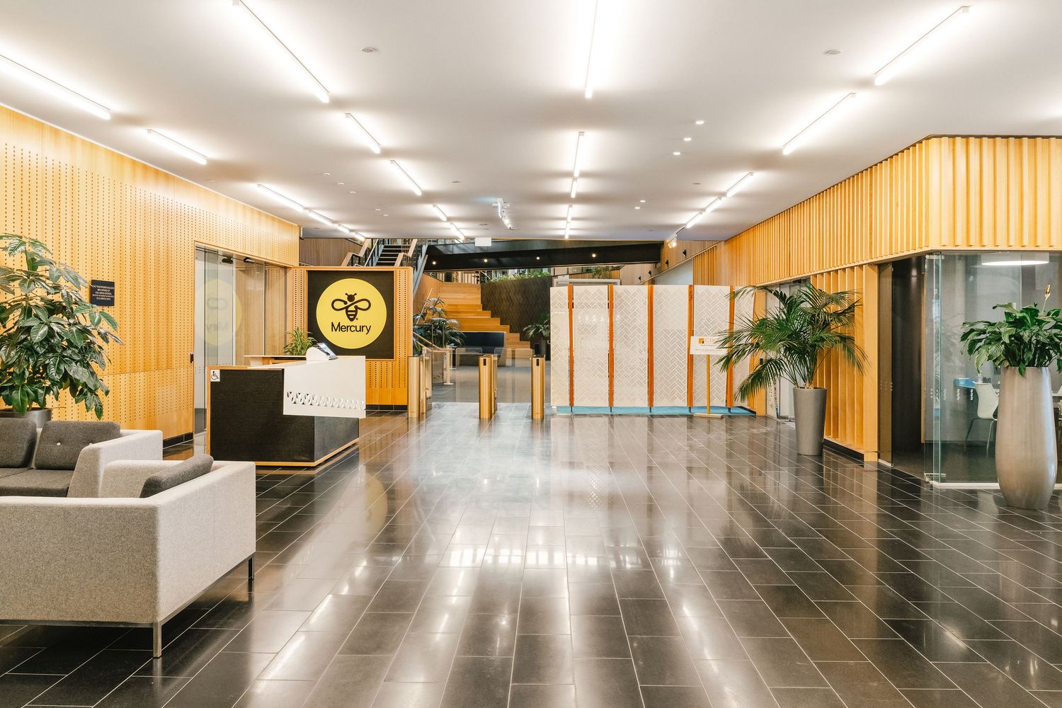 Modern office lobby with wood paneled walls, sleek furniture, potted plants and glossy dark floors.