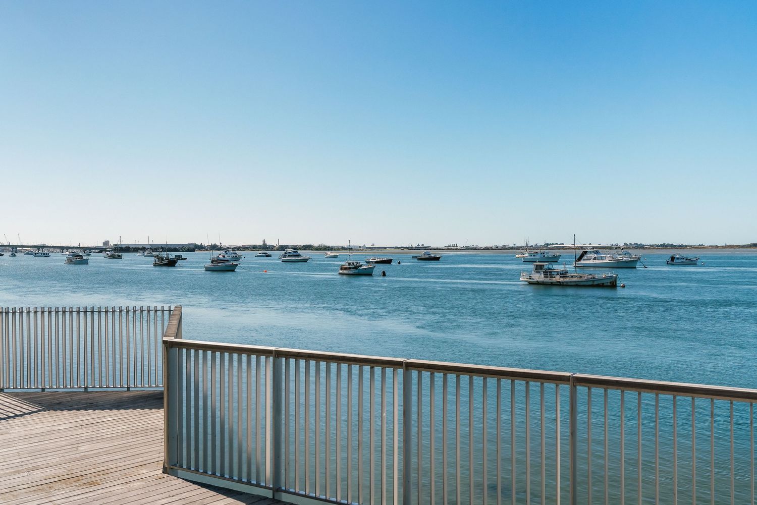Peaceful harbor scene with numerous sailboats anchored in calm blue waters under a clear sky at dusk.