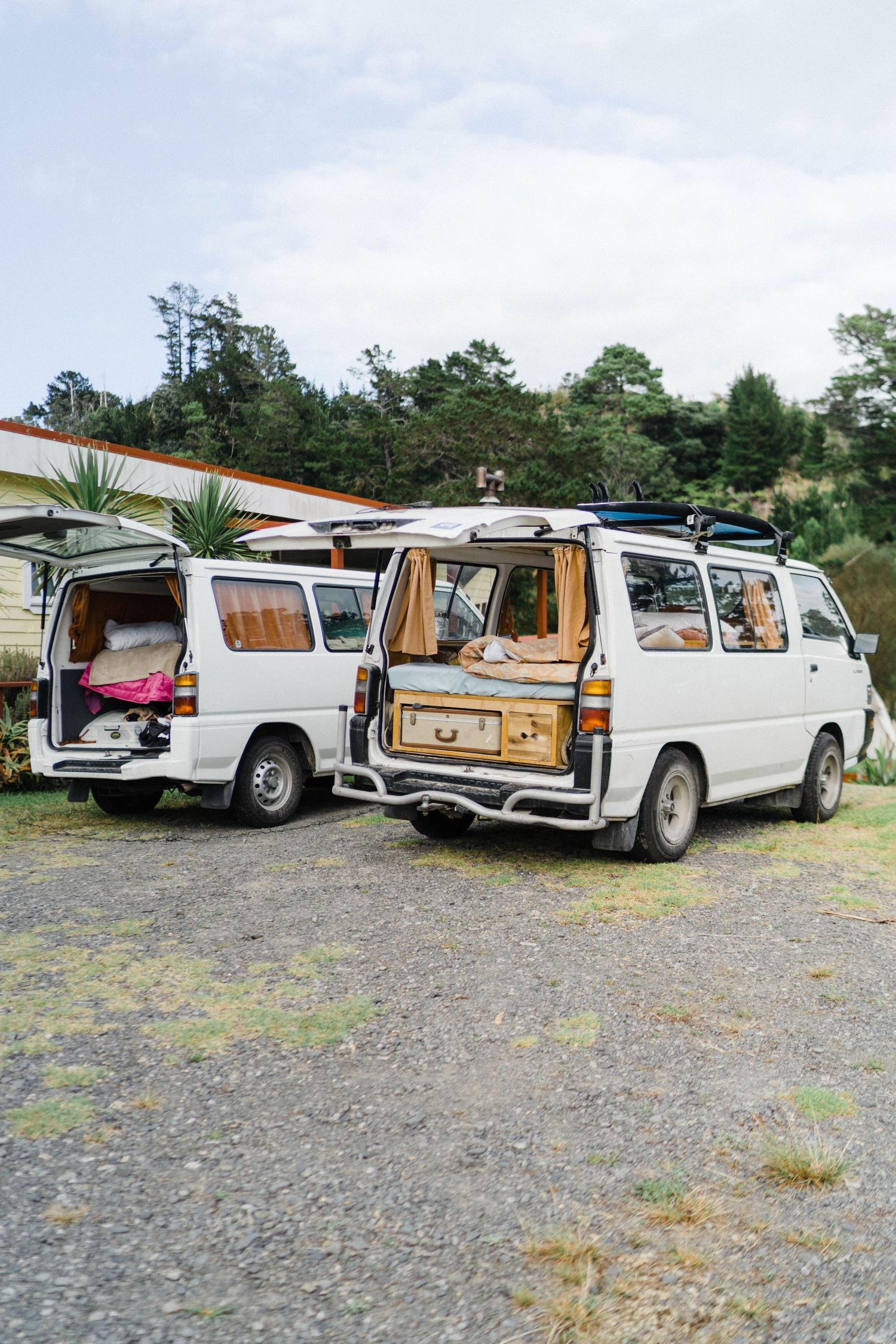 Two white vintage vans parked side by side with open doors showing camping setups inside.