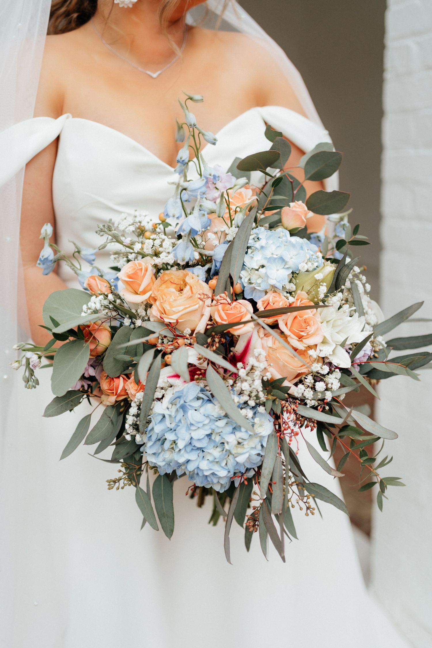 Close-up of stunning bridal bouquet with blue hydrangeas, peach roses, and eucalyptus foliage.
