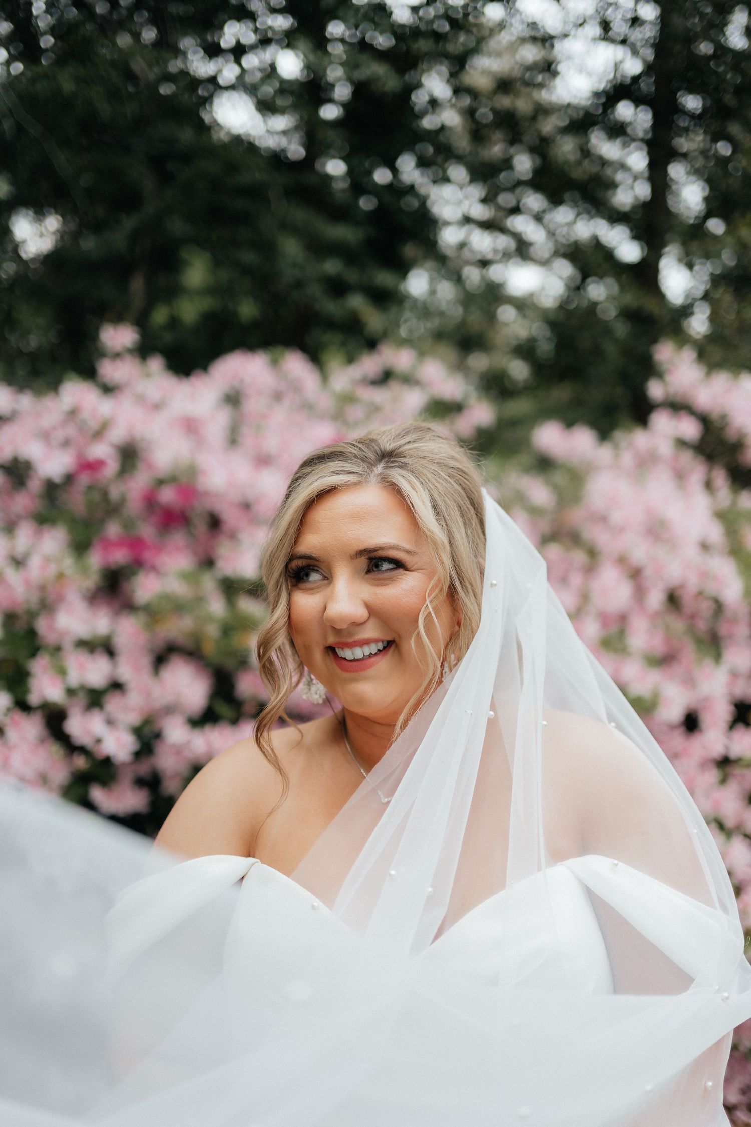 Wedding portrait featuring a flowing white dress and veil against a backdrop of blooming pink azaleas.
