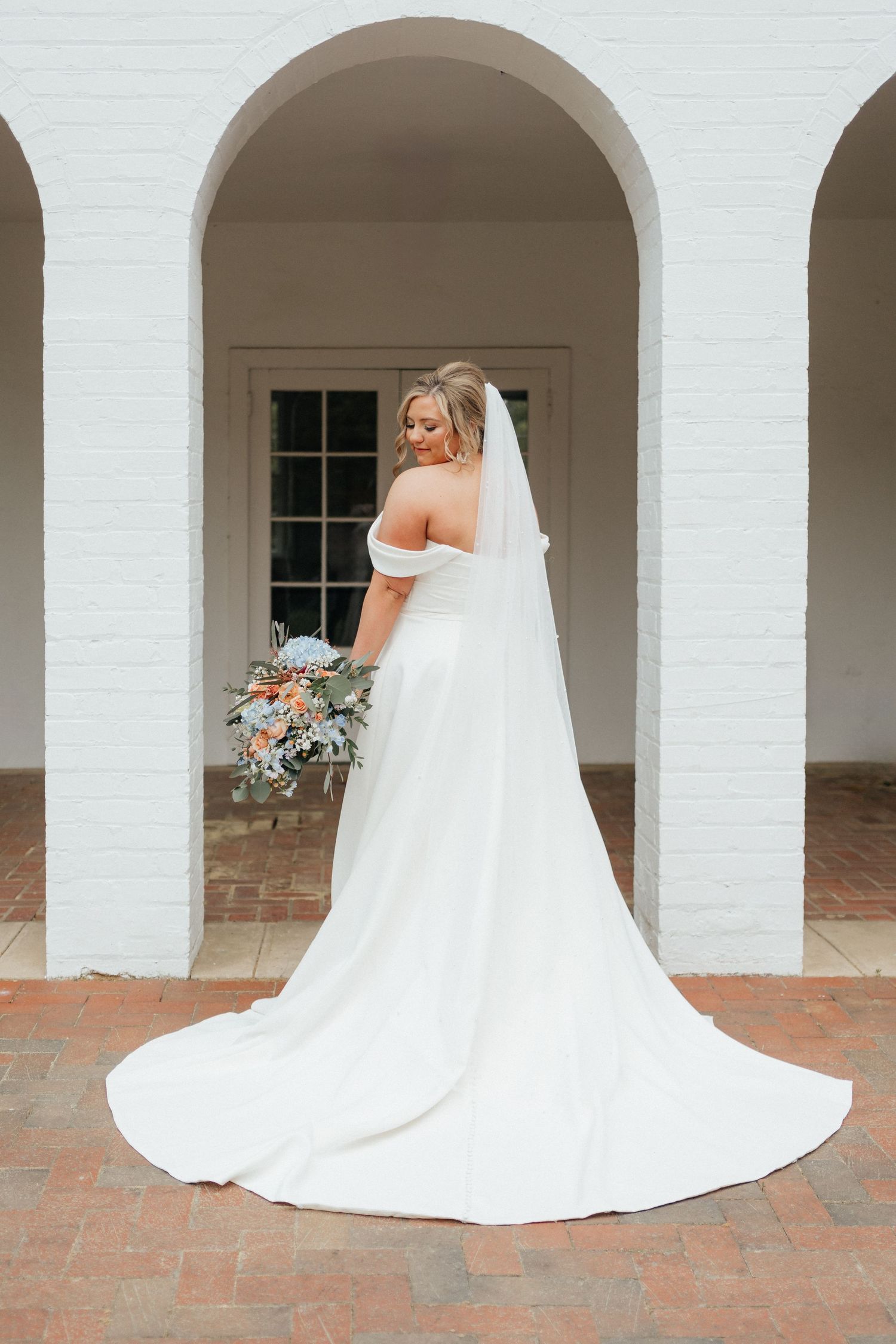 Full length back view of bride in classic white gown with long train and veil under arched doorway.