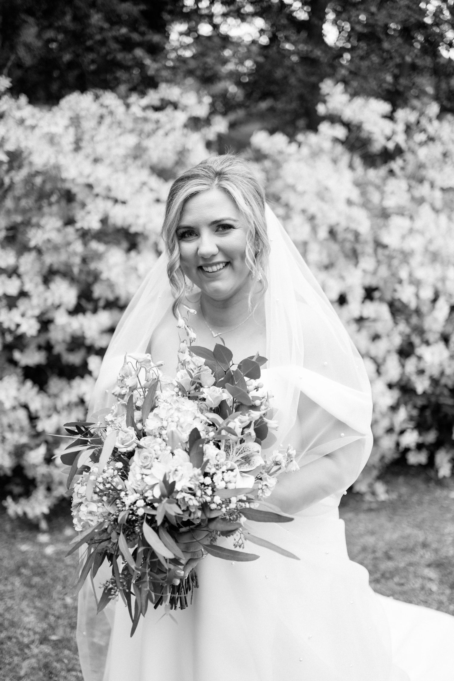 Black and white wedding photography series showing elegant bouquet and flowing veil in garden setting.