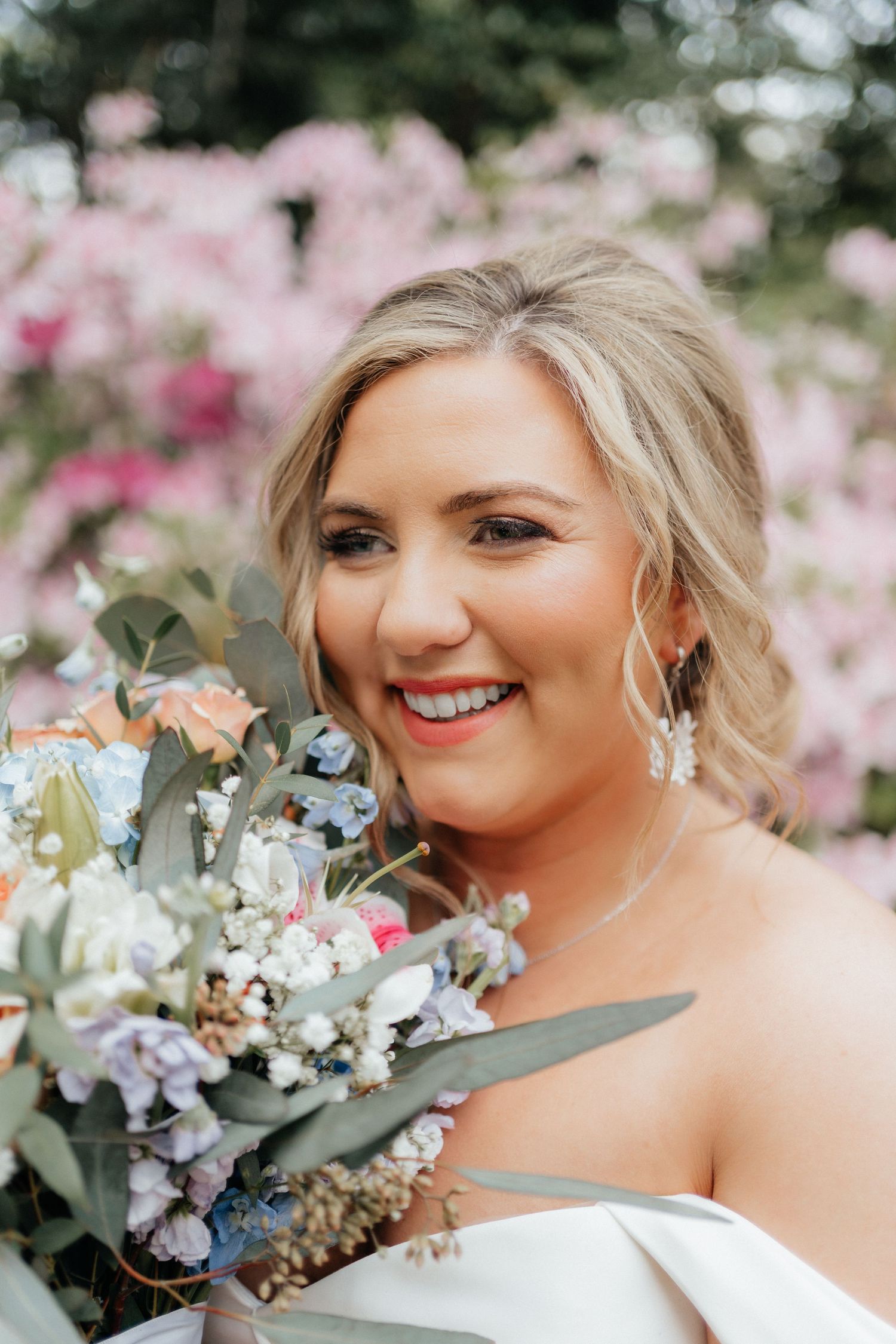 Bridal portrait with delicate bouquet featuring eucalyptus and pastel flowers against pink cherry blossoms.