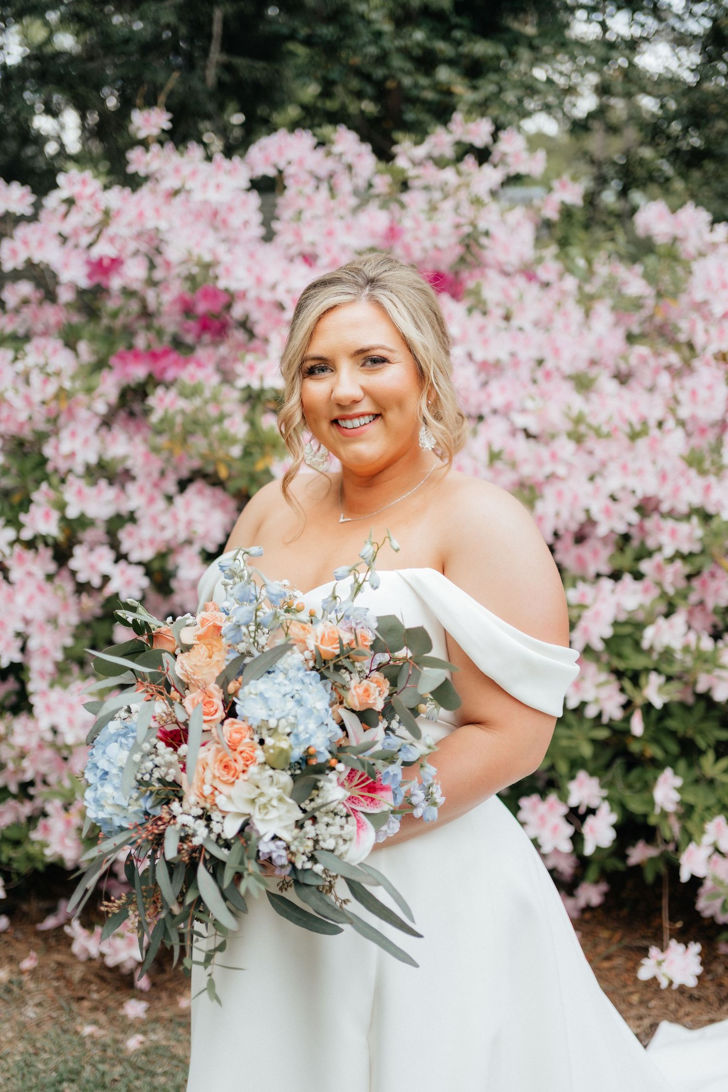 Spring wedding portrait with blooming pink azaleas and coordinating peach and blue bouquet.