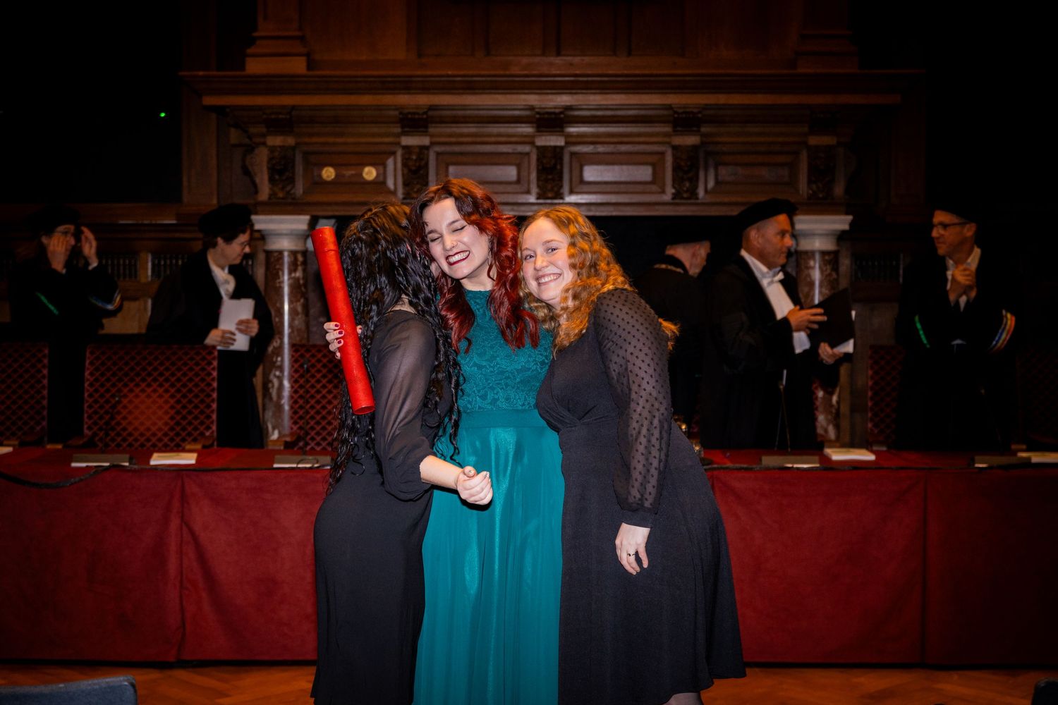 People gathered in a dimly lit formal venue with red velvet decor.