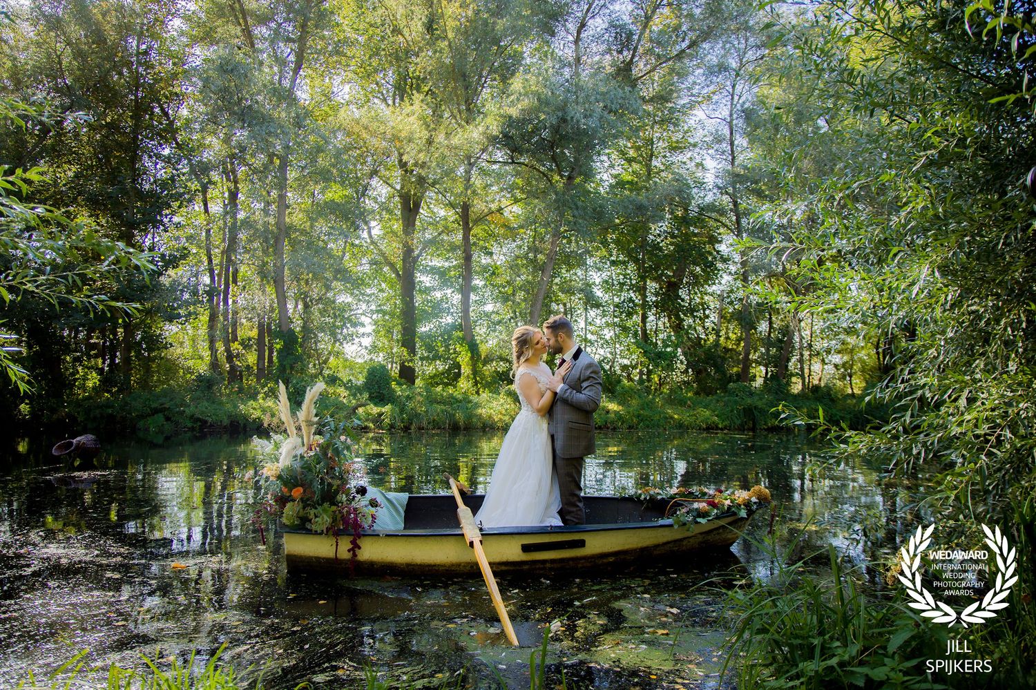 Couple posing romantically in wooden boat on serene woodland pond.