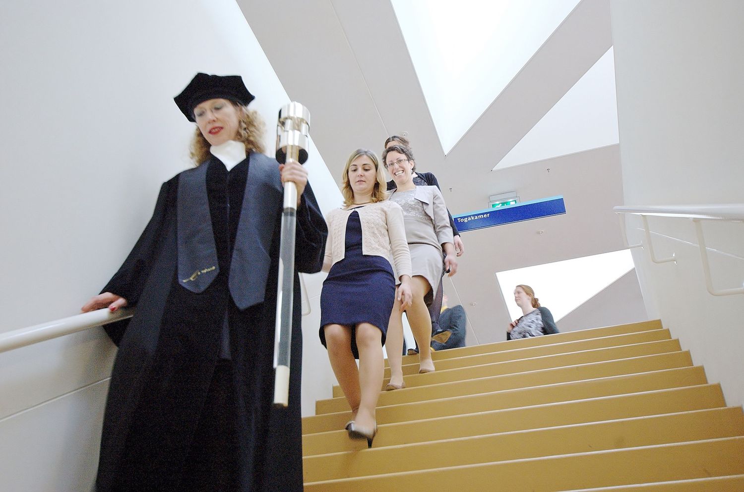 Students wearing black and white clothing walk up and down a modern staircase in an artistic sequence.
