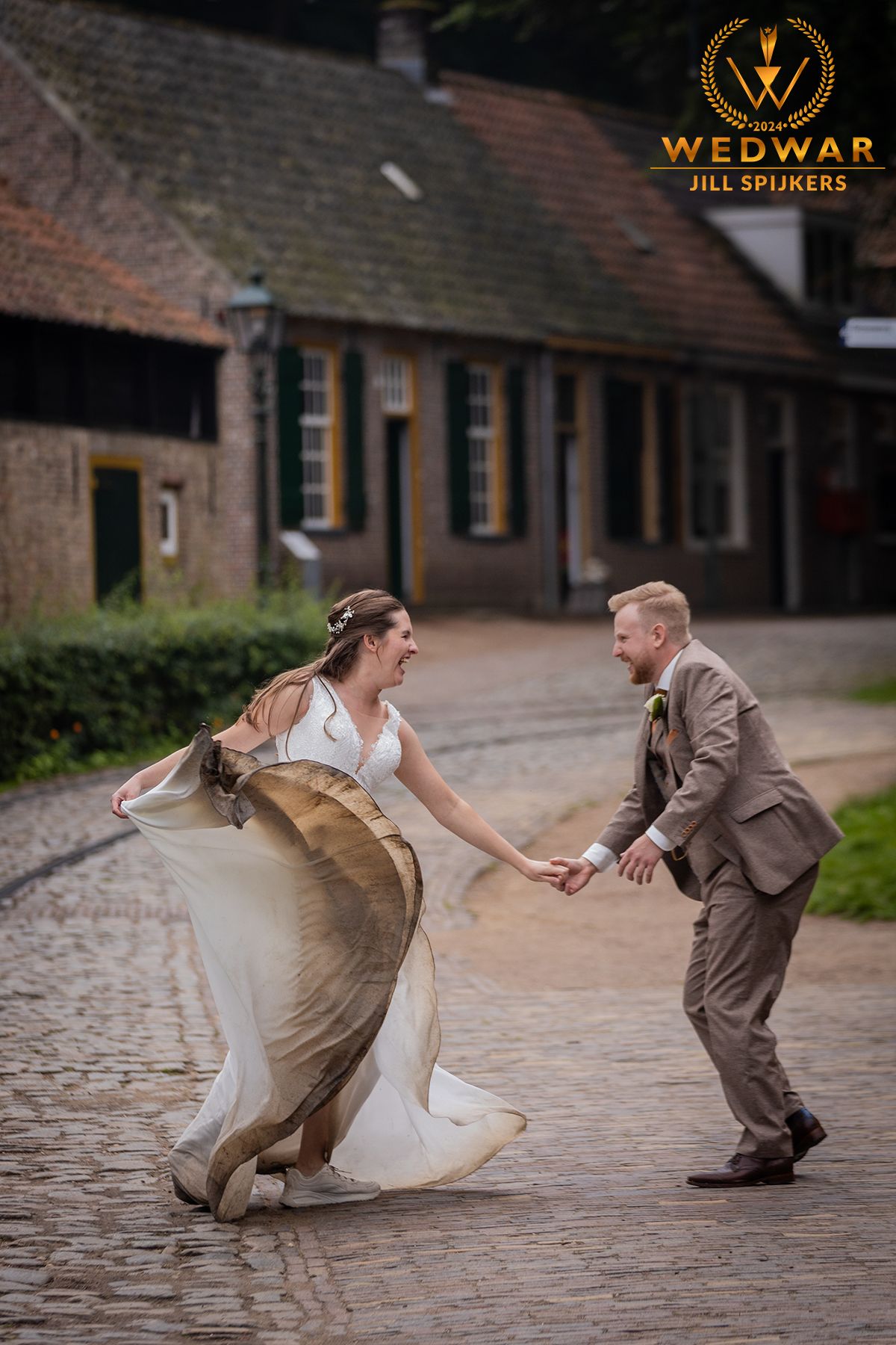 Couple dances playfully on cobblestone street in front of rustic building.