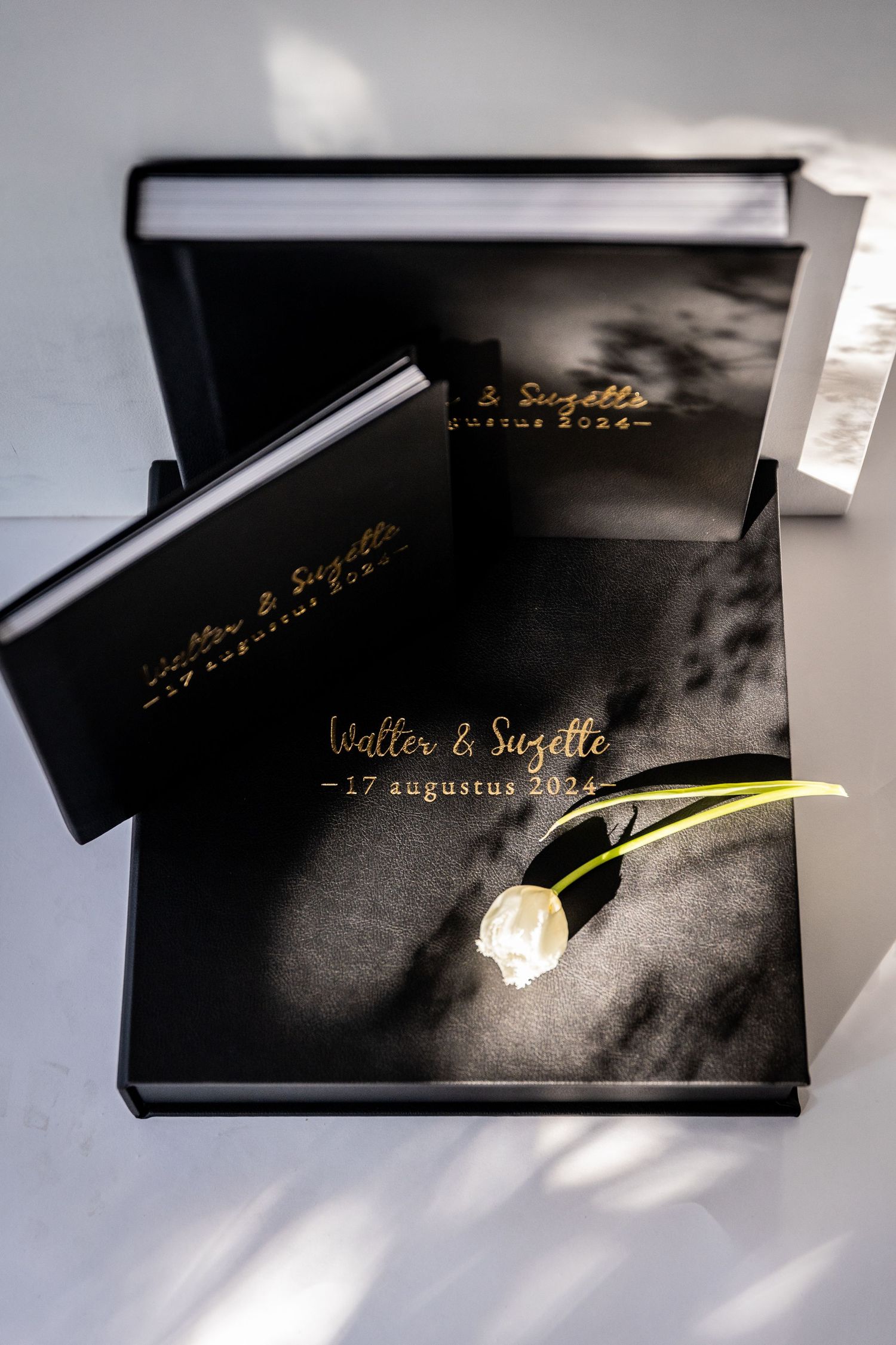 Elegant black wedding photo album with gold text and single white rose.