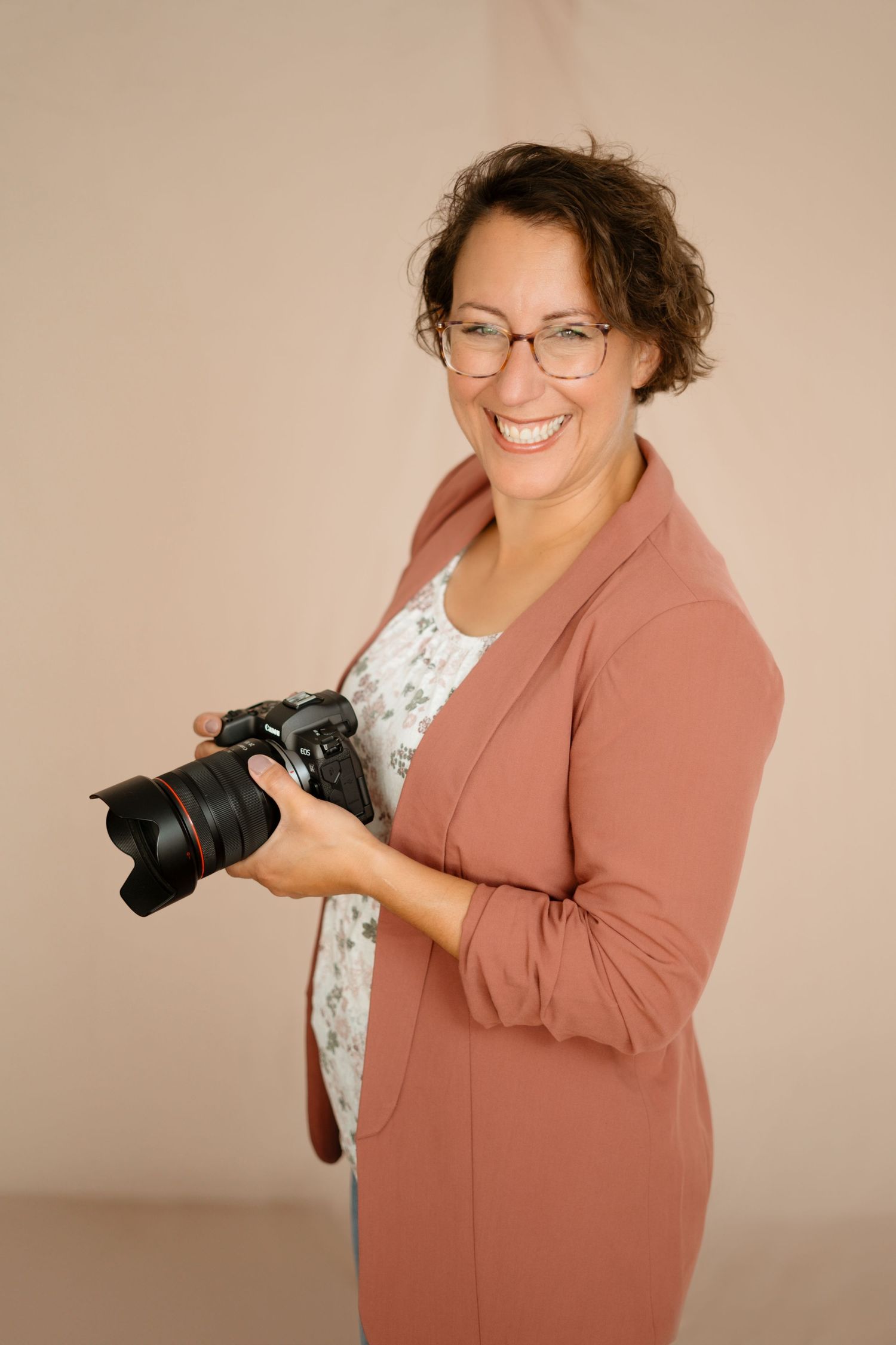 A photographer in a peach blazer demonstrating various poses with camera equipment.