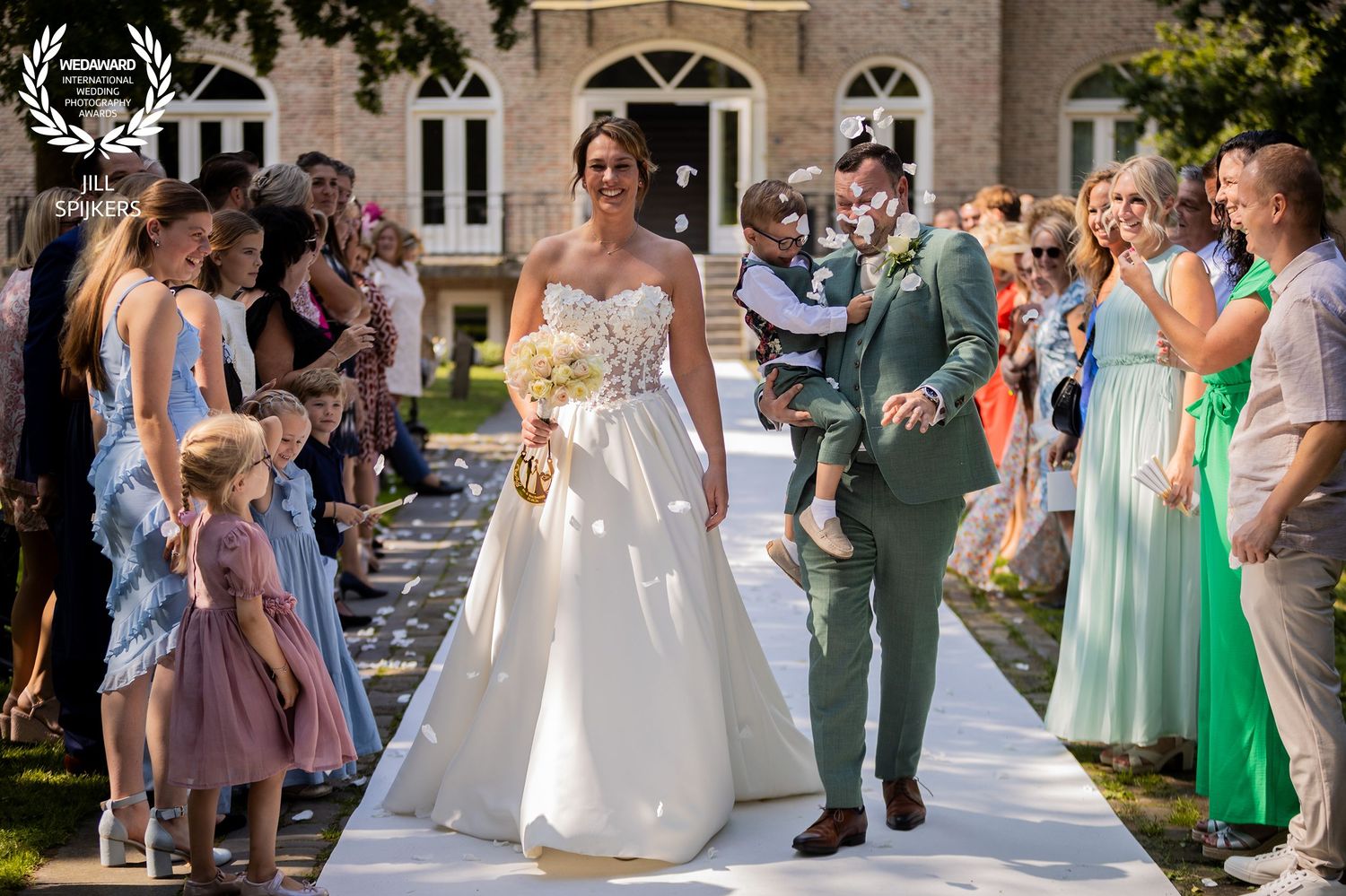 Wedding ceremony processional on white aisle runner with guests in colorful attire.