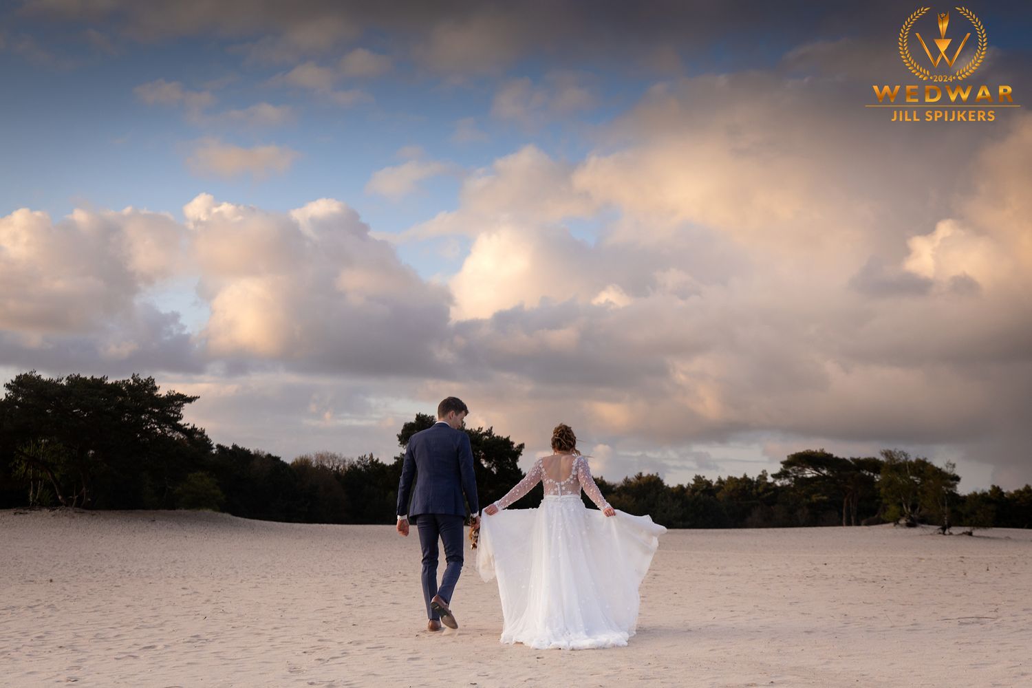 Couple walking hand in hand on beach at sunset with dramatic clouds.