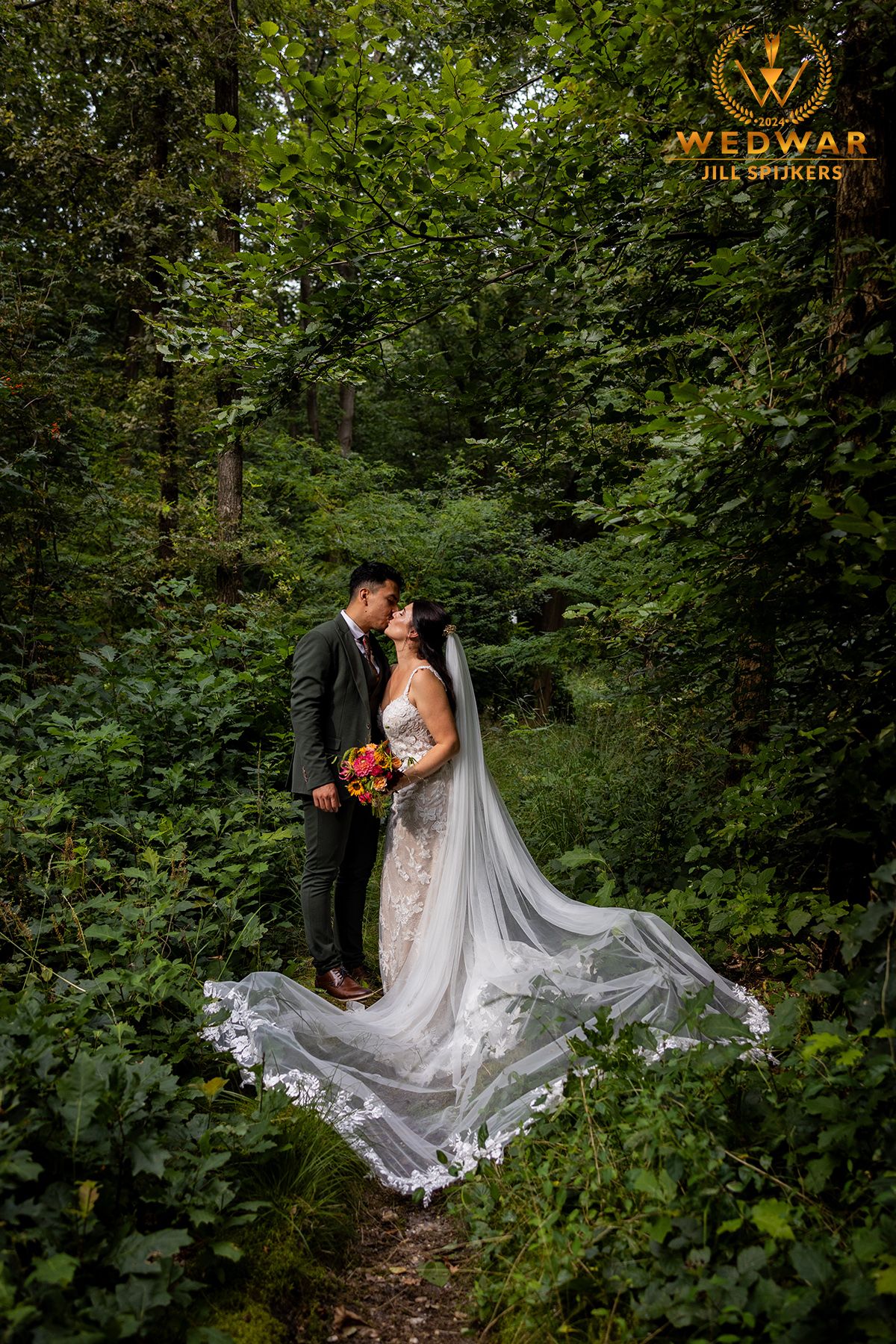 Wedding couple poses on forest path with flowing white veil and bouquet.