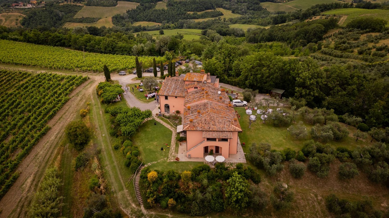 Aerial panoramic view of a picturesque Tuscan countryside with vineyards, olive groves, and red-roofed villas.