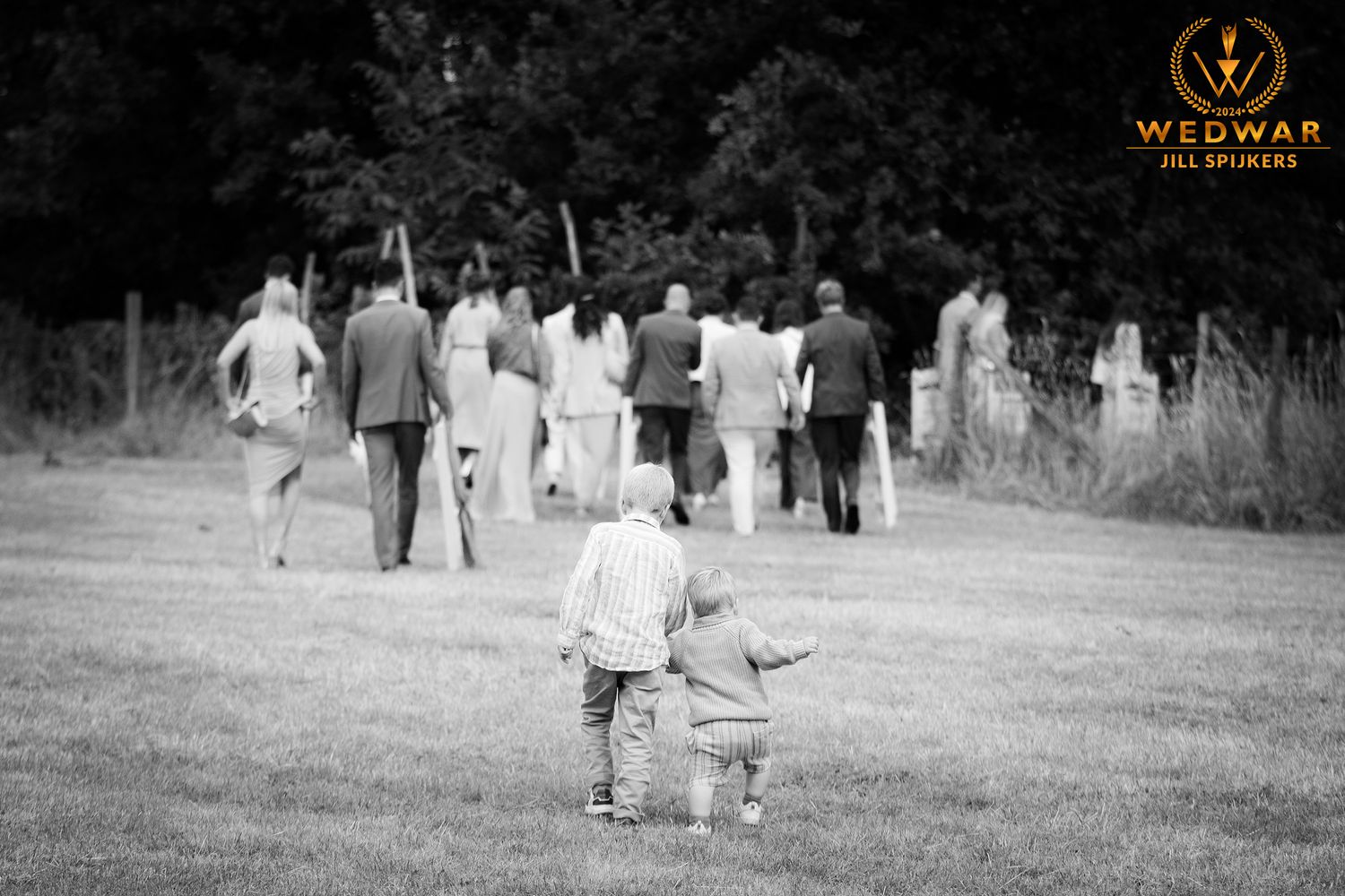 Black and white photo of children following wedding party across field.