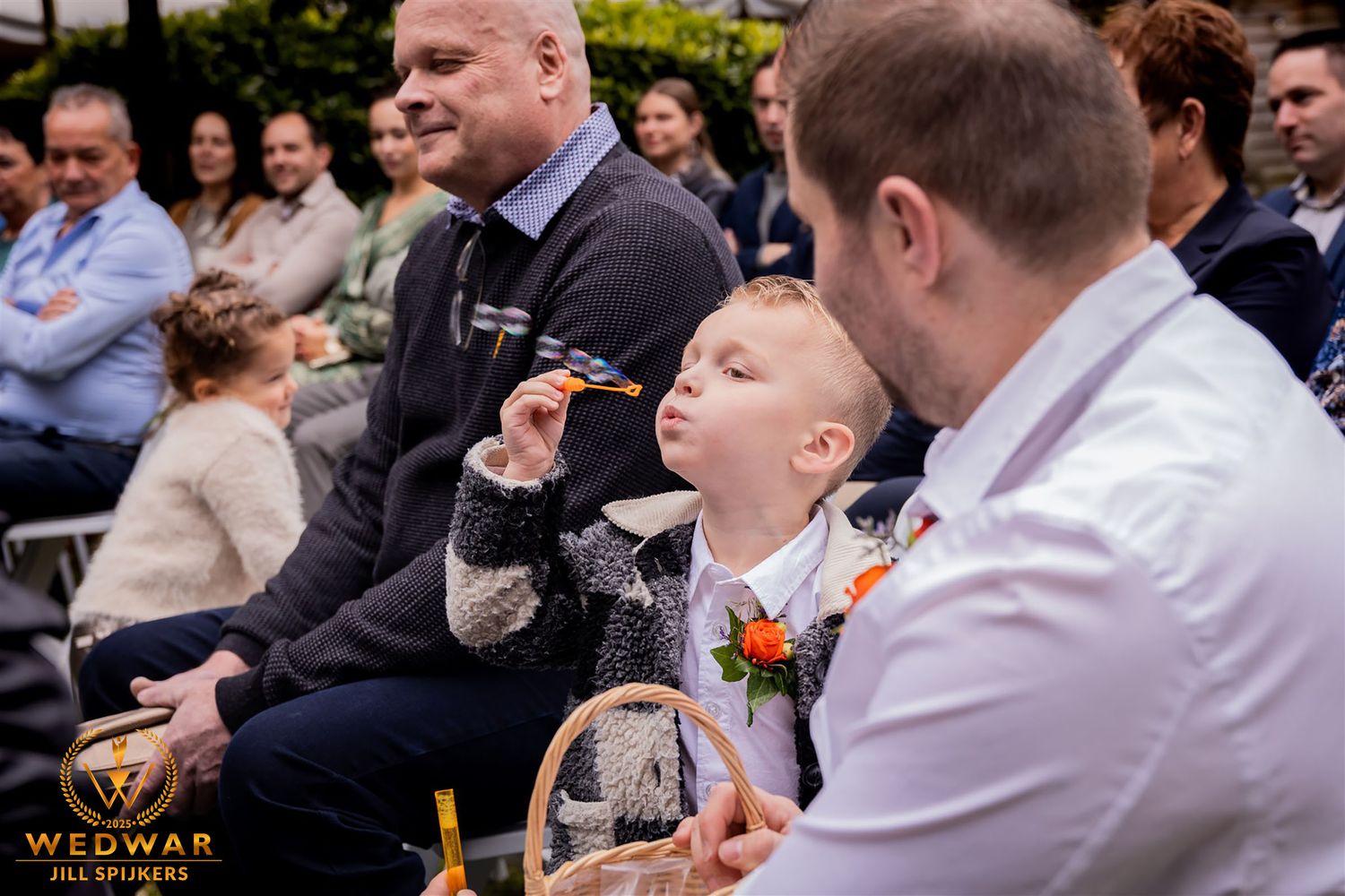 A young guest at a wedding ceremony playfully blows bubbles while seated in the audience.