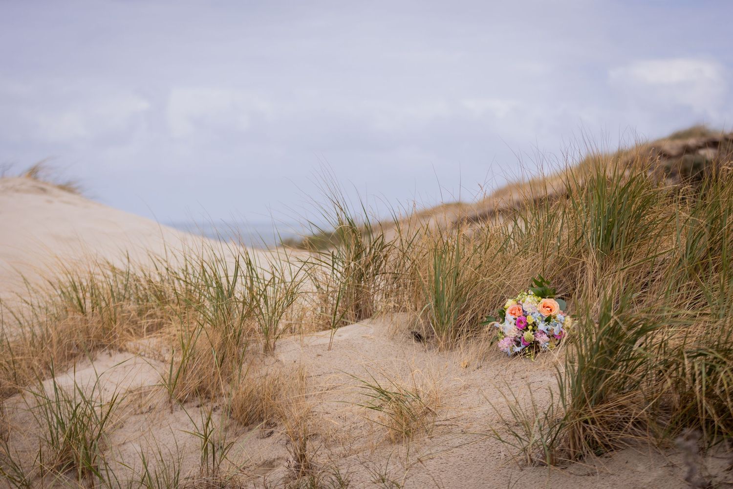 Beach wedding ceremony among sand dunes with tall grass and soft light from the cloudy sky.