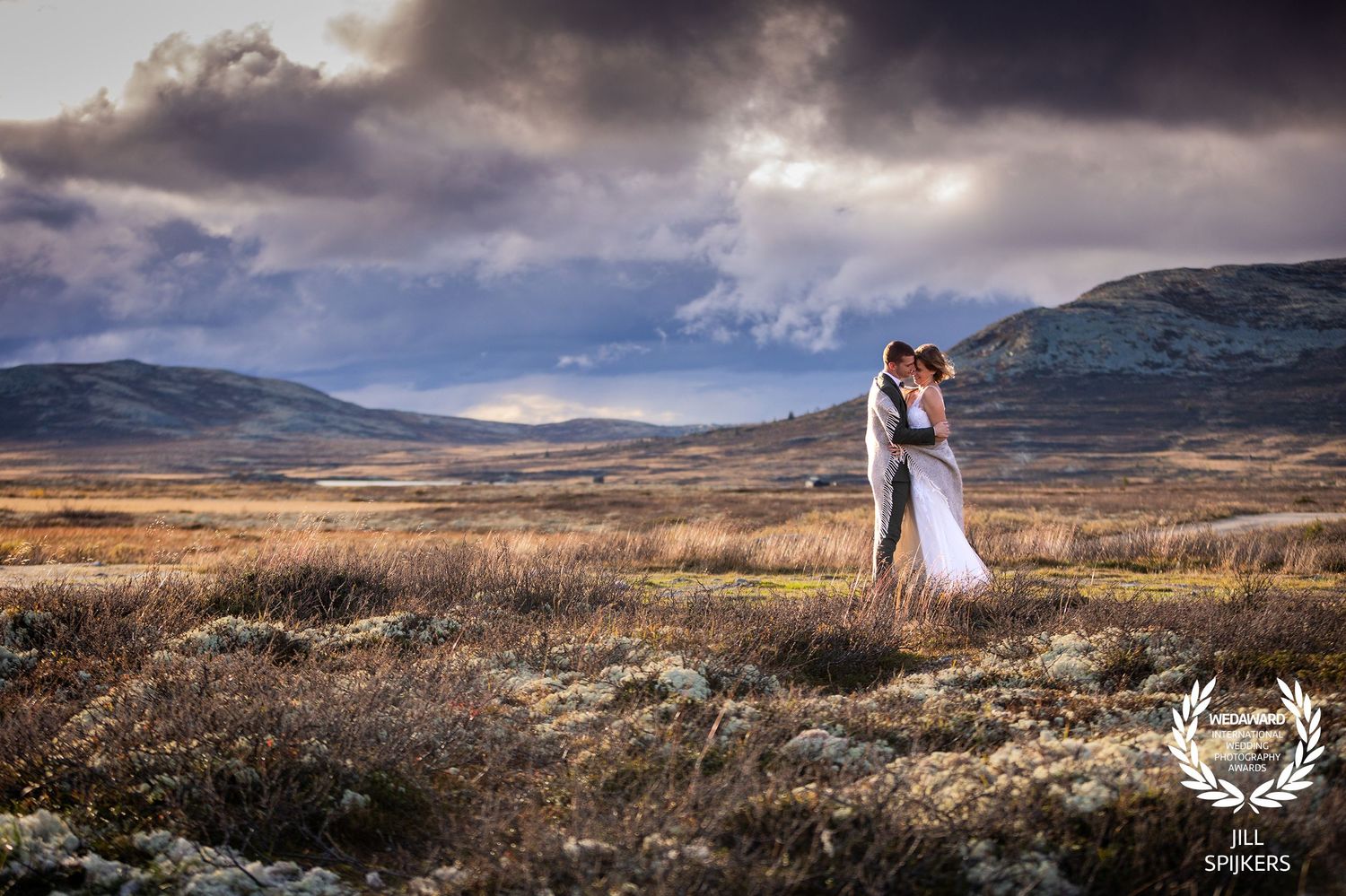 Dramatic wedding photo with couple standing in rugged mountain landscape under stormy skies.