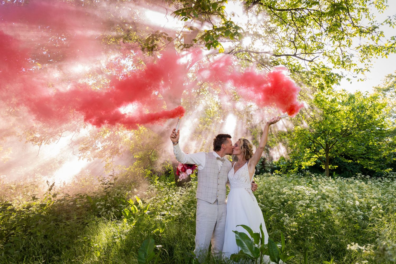 Couple releases red smoke bombs in outdoor wedding photo with dramatic sky.